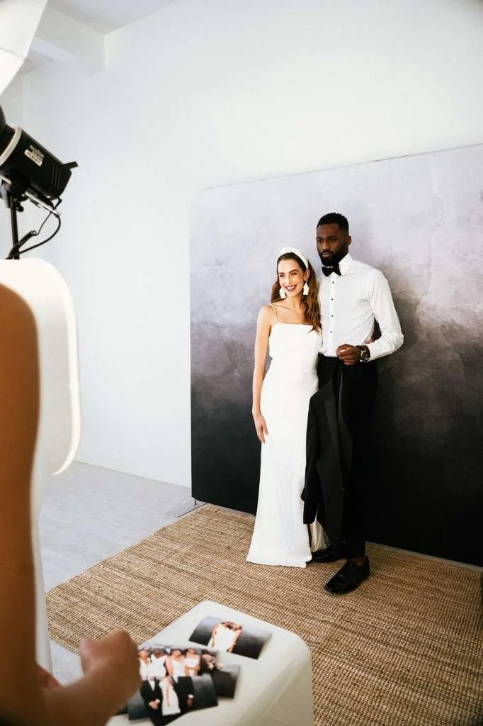 A couple dressed in wedding attire posing for photos in a studio, with a photographer taking their picture.