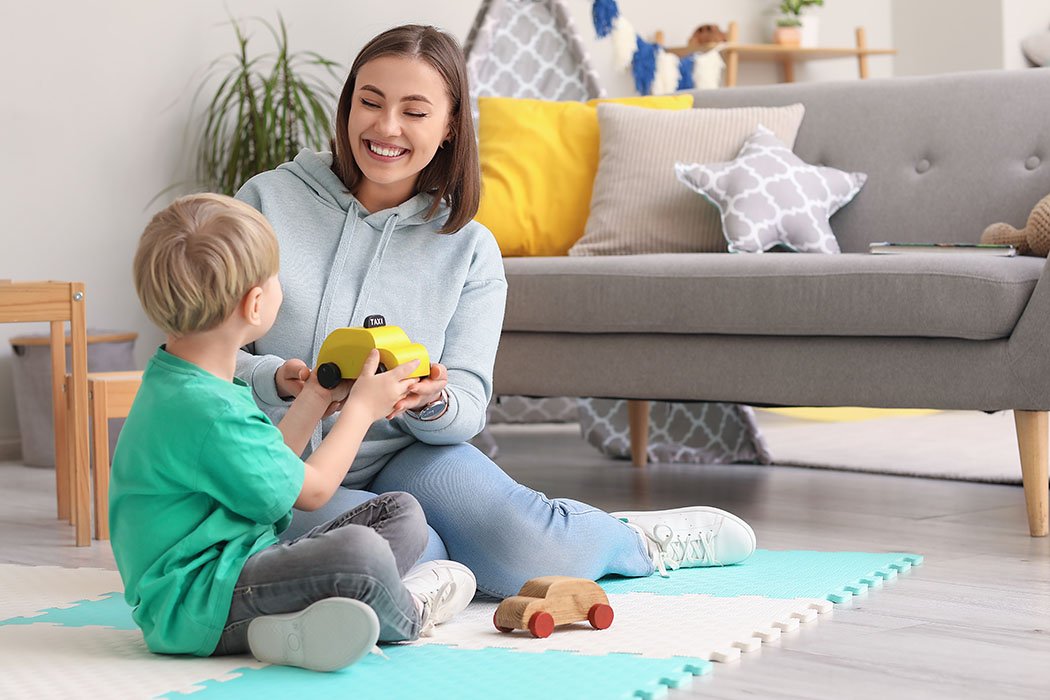 A woman and a young boy playing with a toy taxi in a living room.