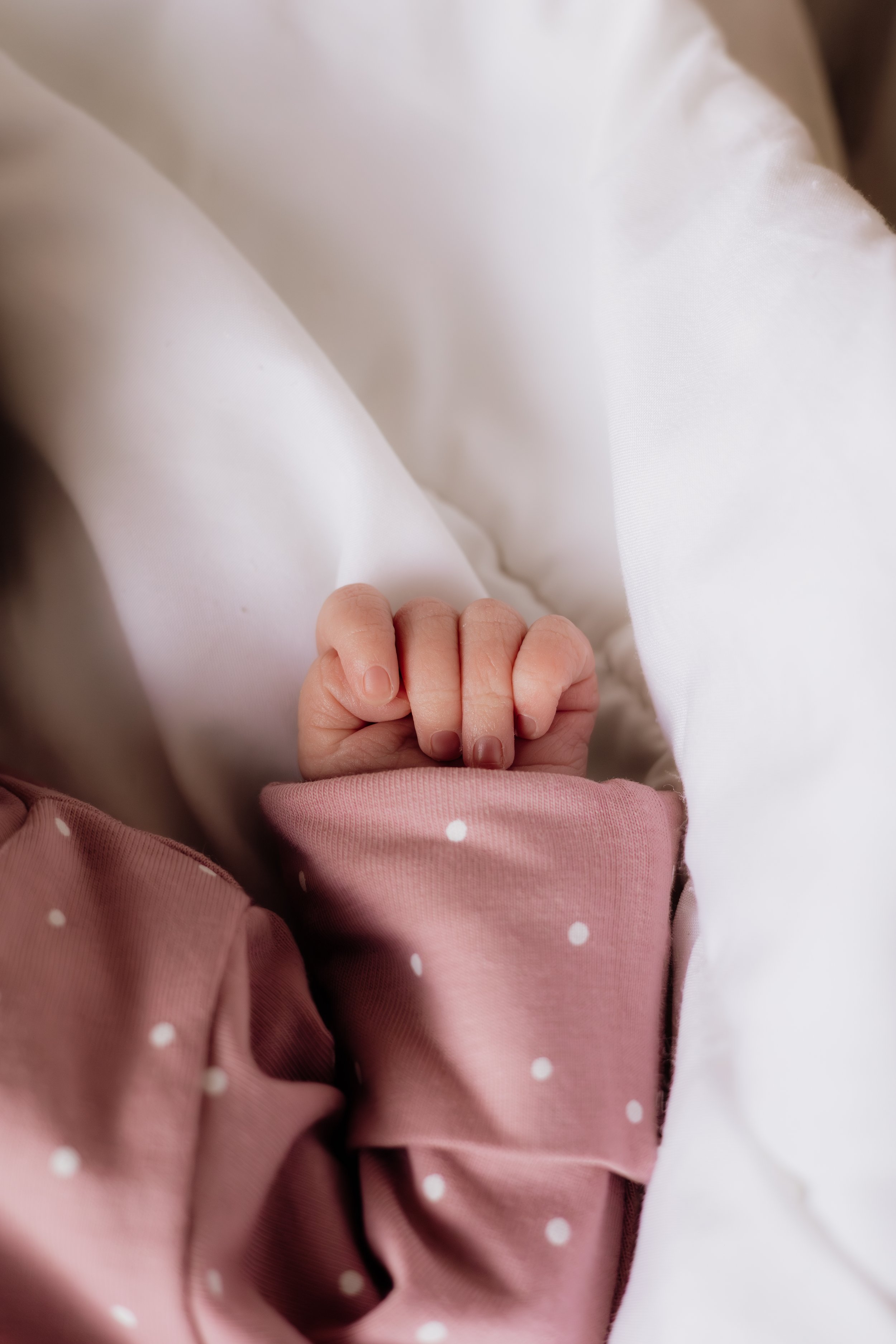 Close-up of a child's hand holding a white cloth, wearing a pink polka dot sweater.