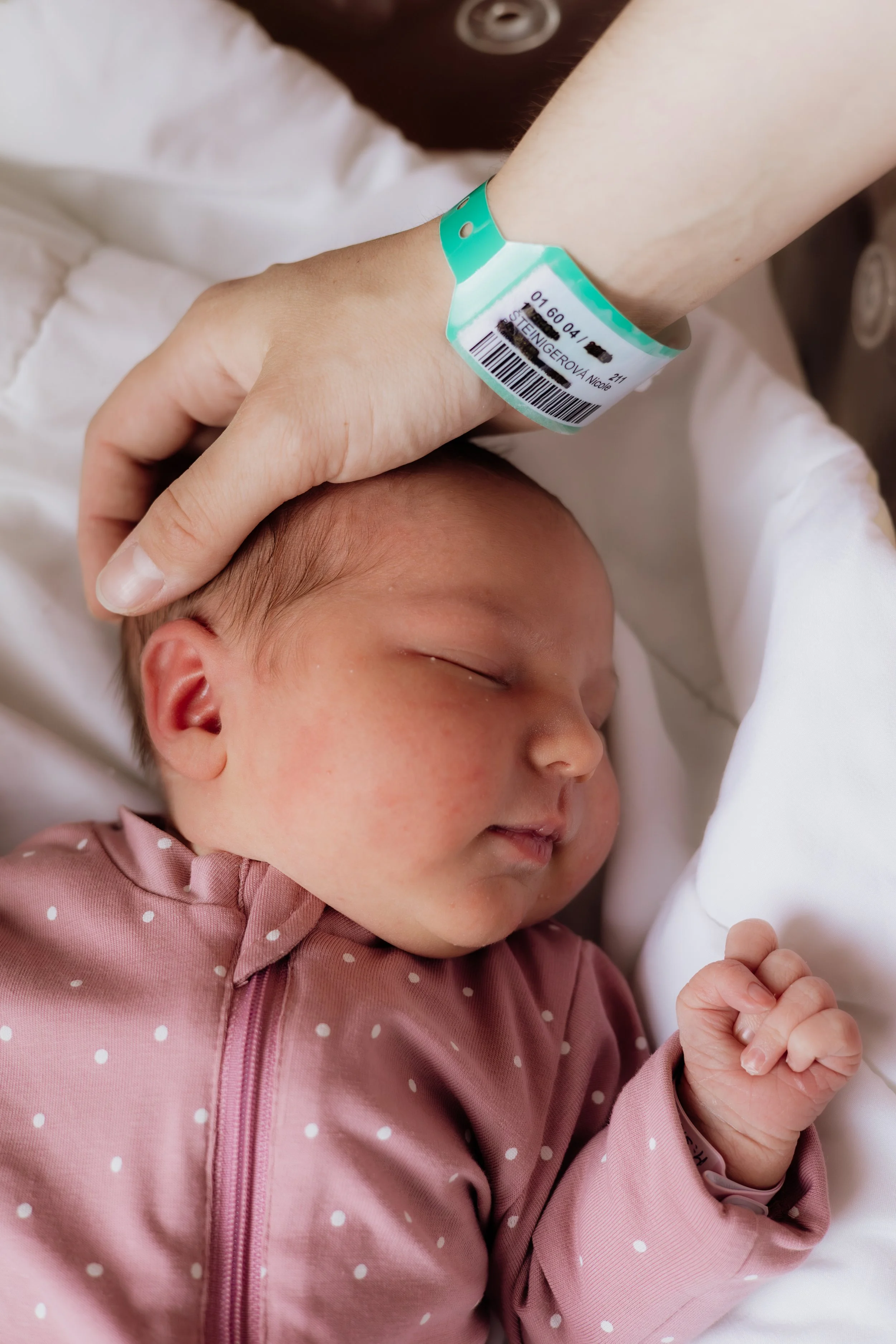 Close-up of a newborn baby sleeping peacefully with an oxygen wristband on her wrist, dressed in a pink dotted outfit.