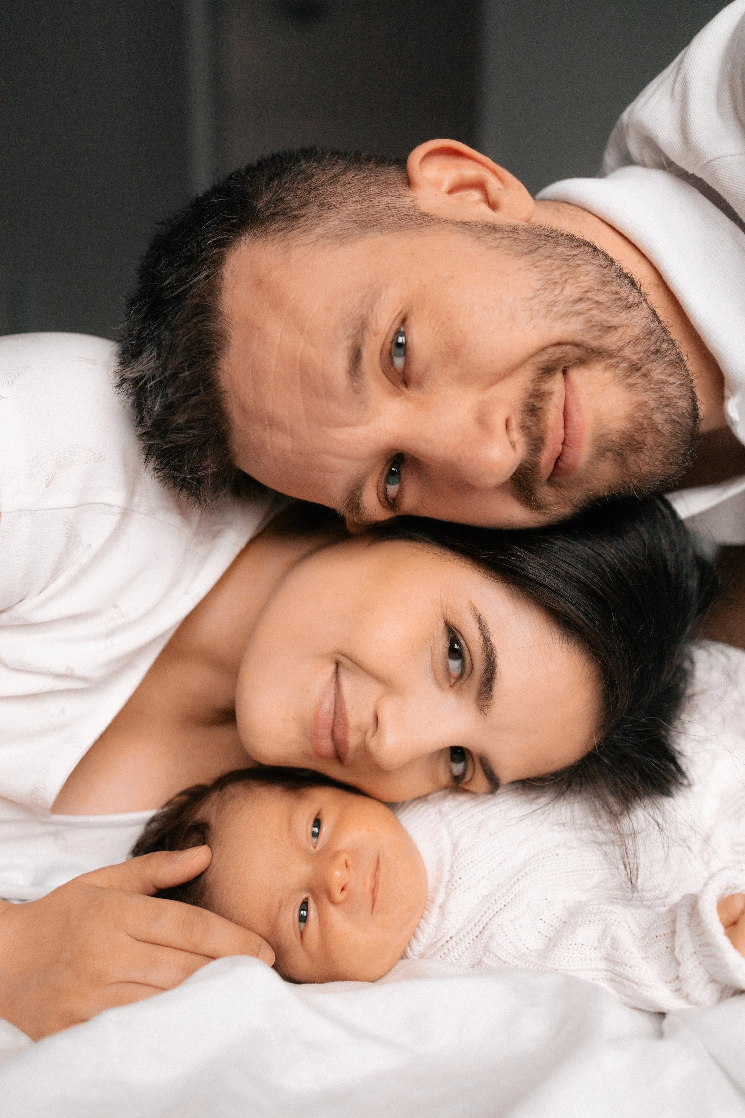 A man lying down with a woman and a baby, all relaxing together, close-up shot of their faces.