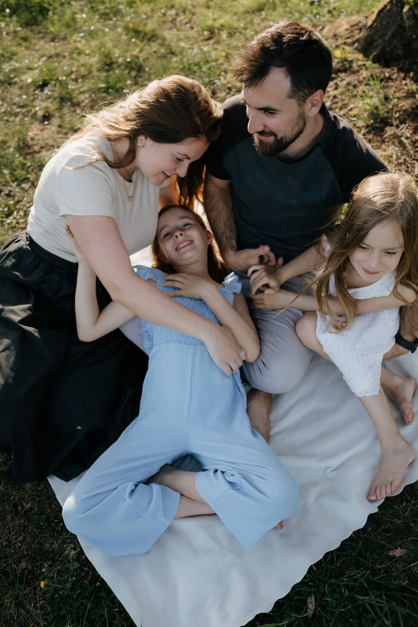 Family lying on a blanket outdoors, smiling, and enjoying each other's company.