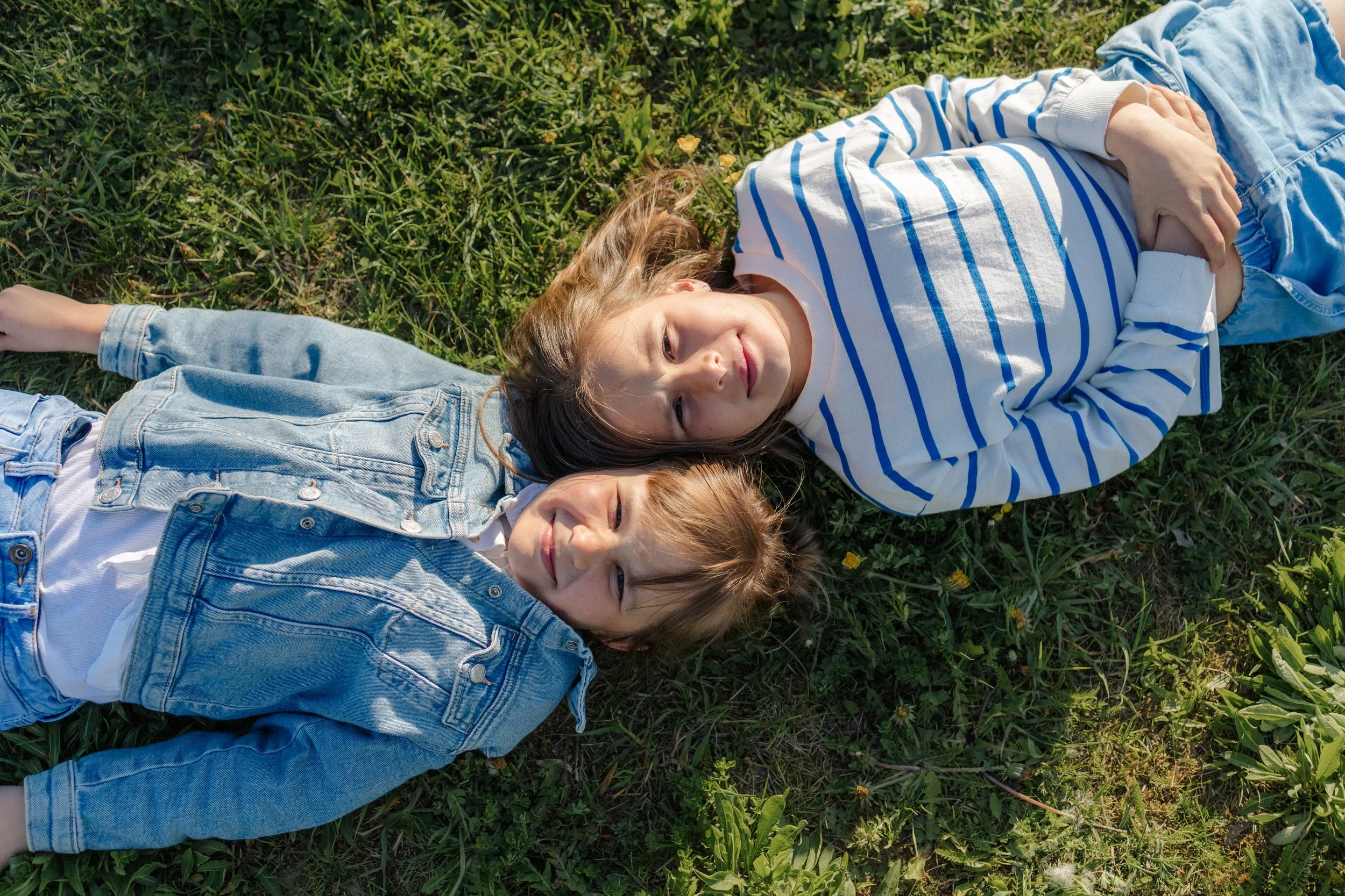 Three children lying on grass outdoors, smiling and relaxing.