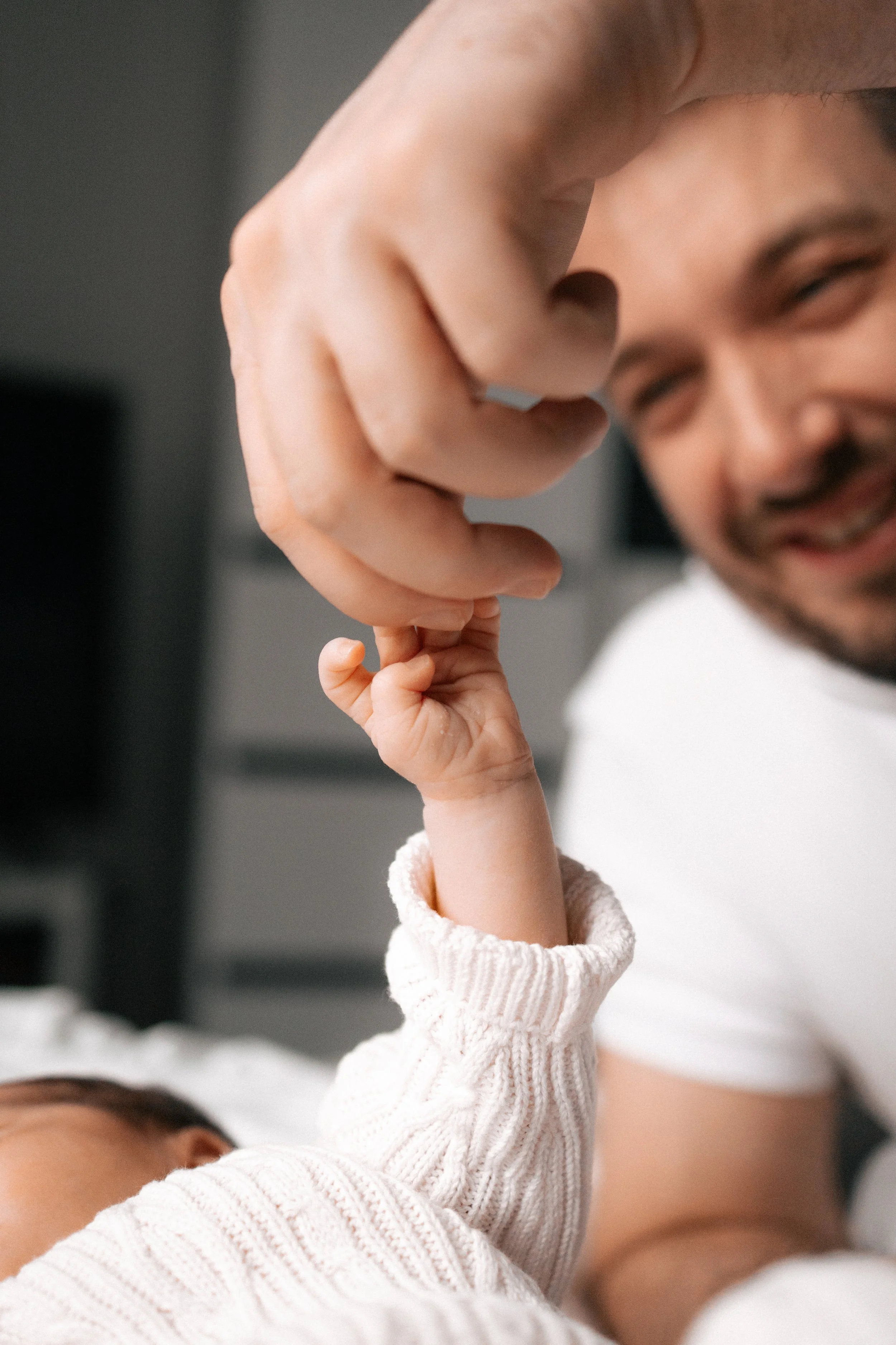A smiling man lying down with a young child raising their hand to touch his face.