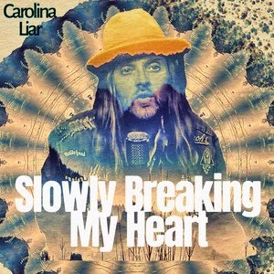 Album cover featuring a portrait of a man with long hair, a beard, wearing a yellow hat, and holding a microphone. Background has radial bursts and a textured surface. Title text reads 'Slowly Breaking My Heart' and artist name 'Carolina Liar'.