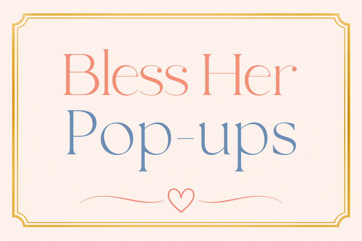 A decorative sign with the message 'Bless Her Pop-ups' in large, colorful text, surrounded by a gold border and a small heart at the bottom.