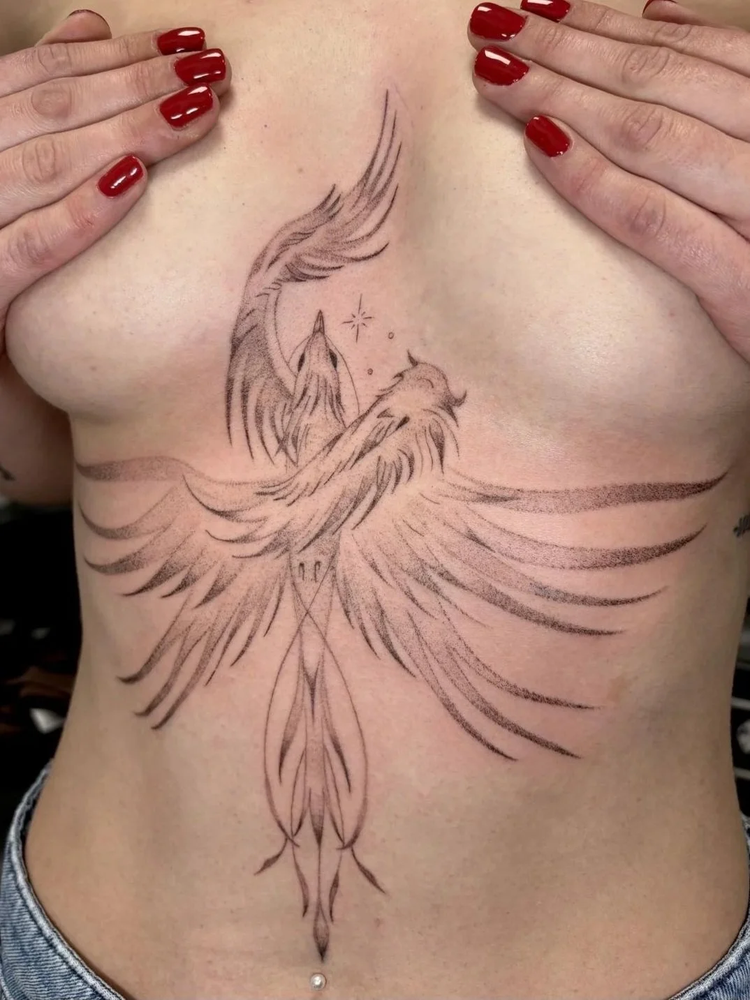 Tattoo eines fliegenden Phönix auf dem Brustbereich einer Person mit roten Nagellack.