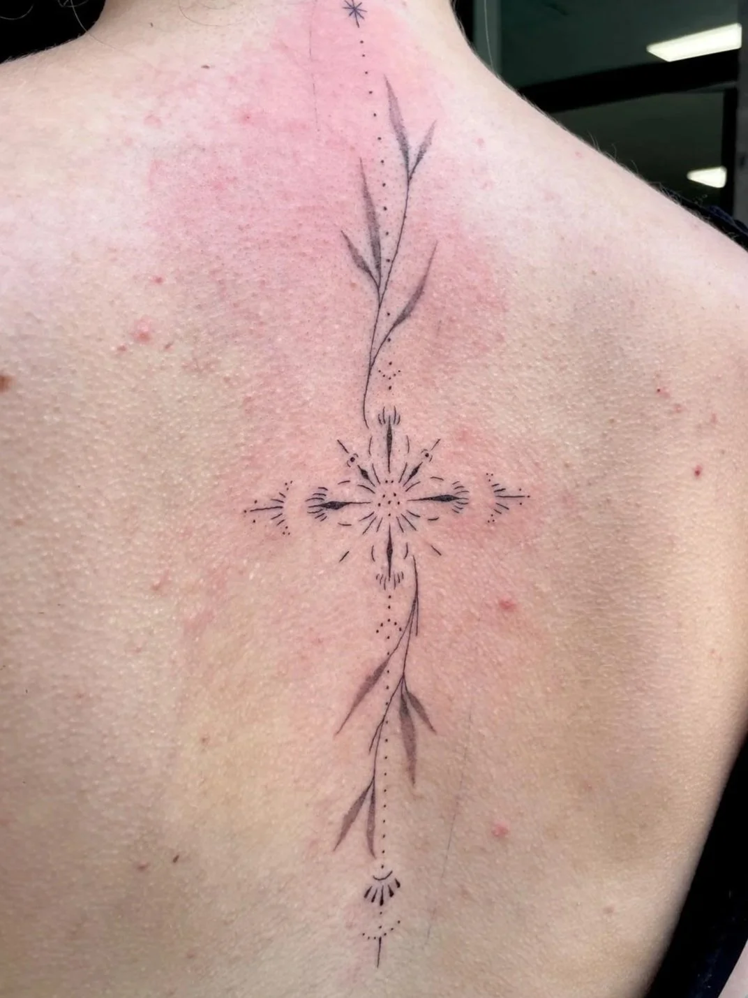 Schwarz-weiße Tattoo eines stilisierten Zweigs mit Blättern und dekorativen Linien auf dem Rücken einer Person.