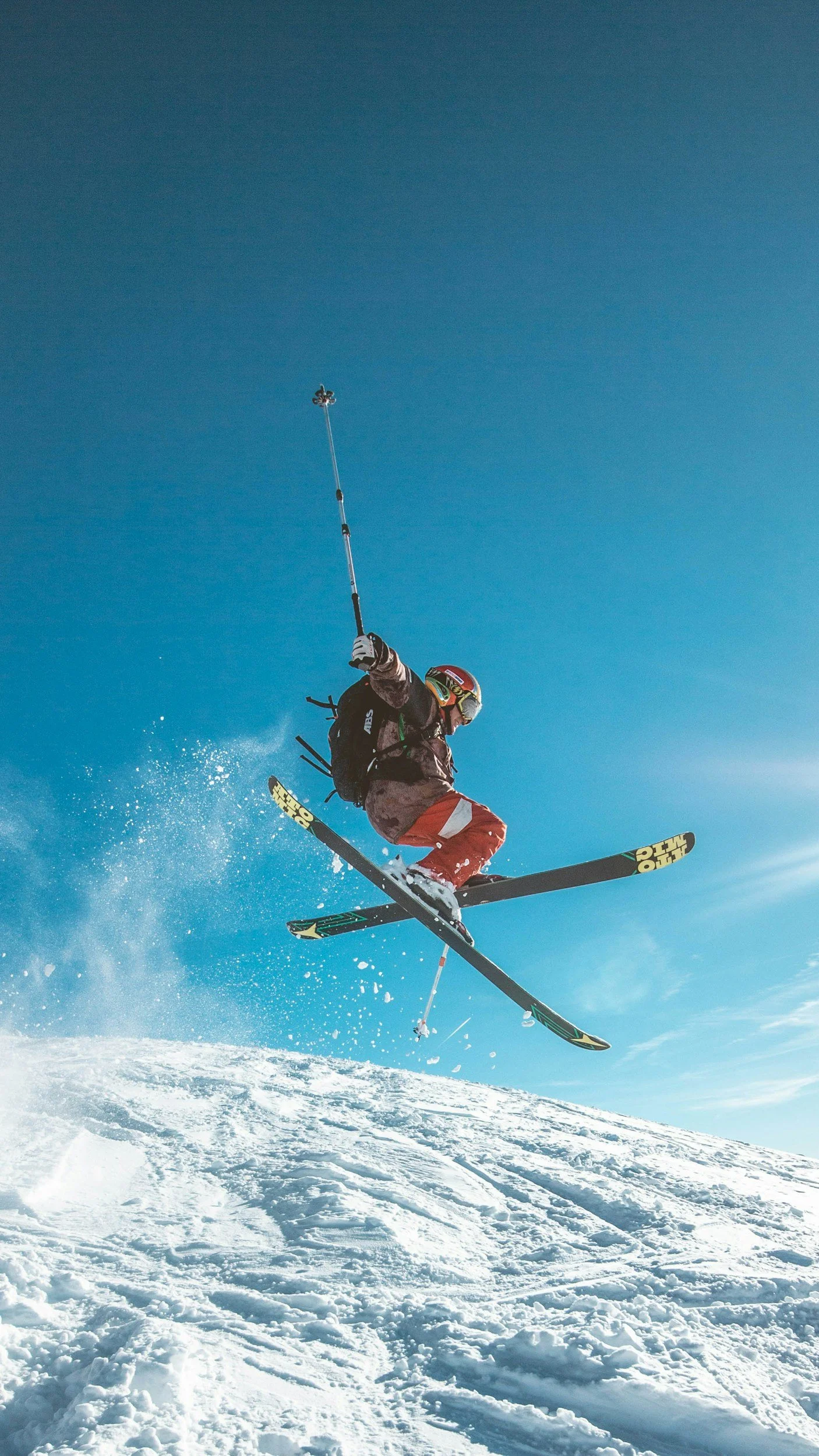 A skier in mid-air performing a jump on a snowy mountain with clear blue sky background.