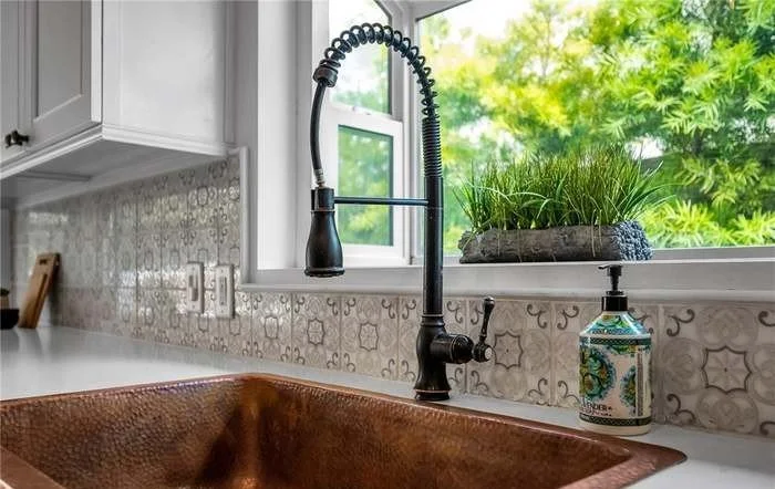 The details make the difference — a hammered copper farmhouse sink and hand-painted marble backsplash elevate this kitchen into a space you'll never want to leave.