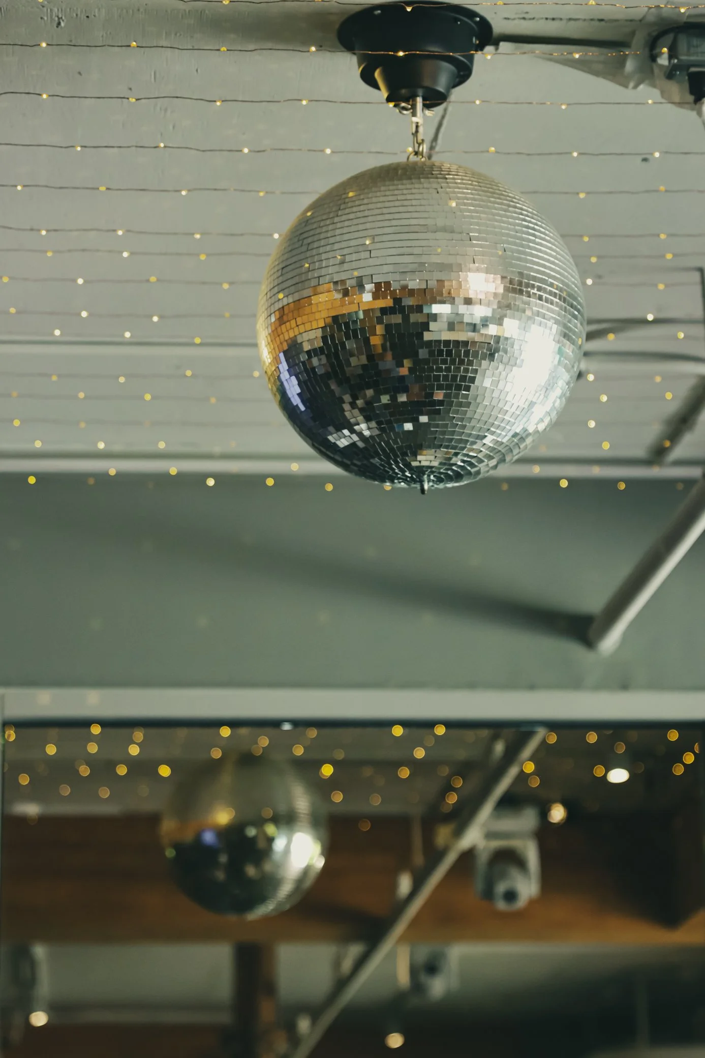 Two disco balls hanging from the ceiling of a room decorated with string lights.