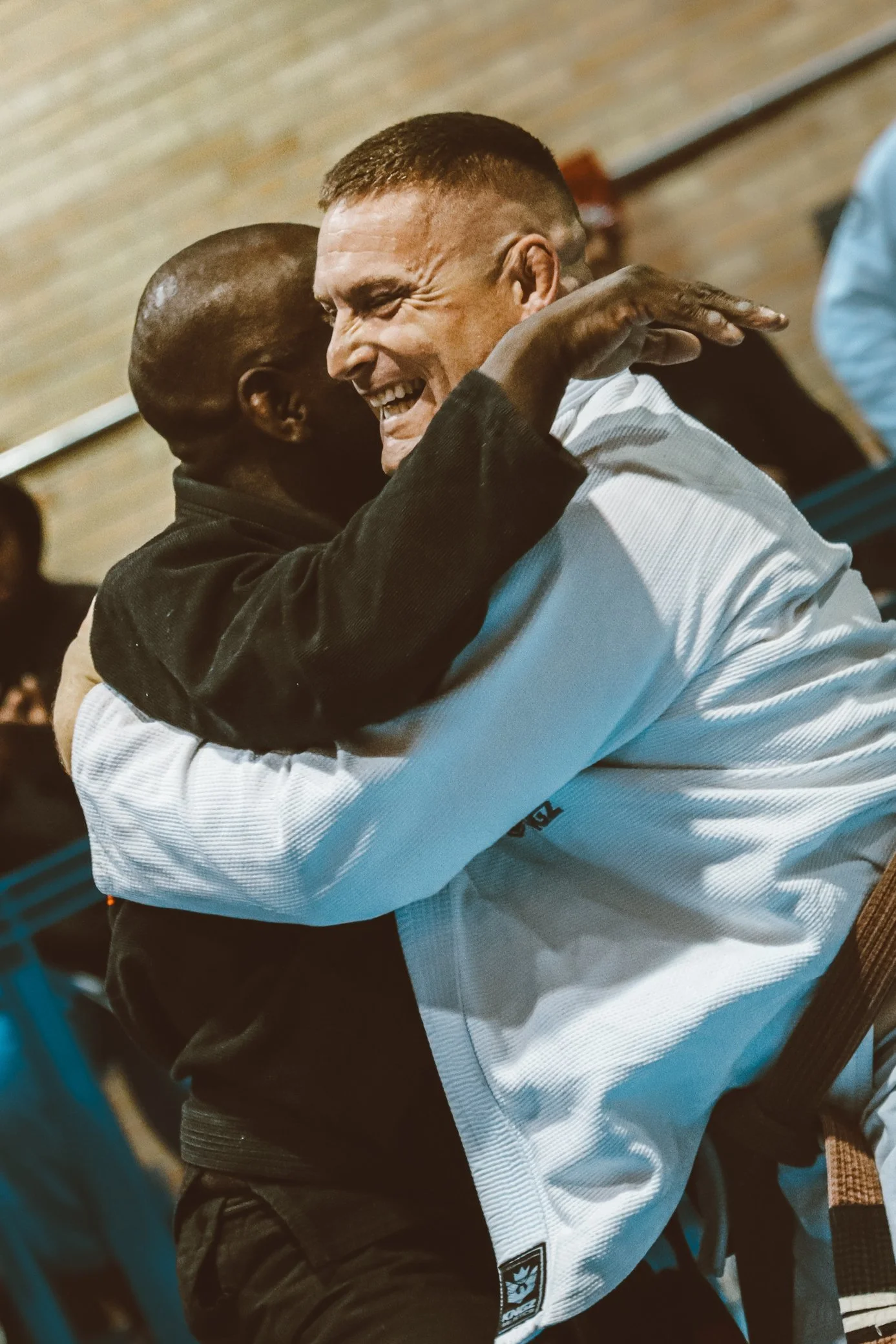 Two men hugging and smiling at each other in a friendly manner inside a building with wooden walls.