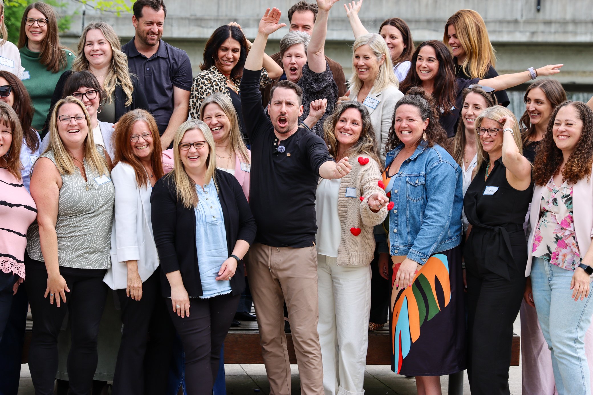 Group of diverse people smiling and celebrating outdoors during the daytime.