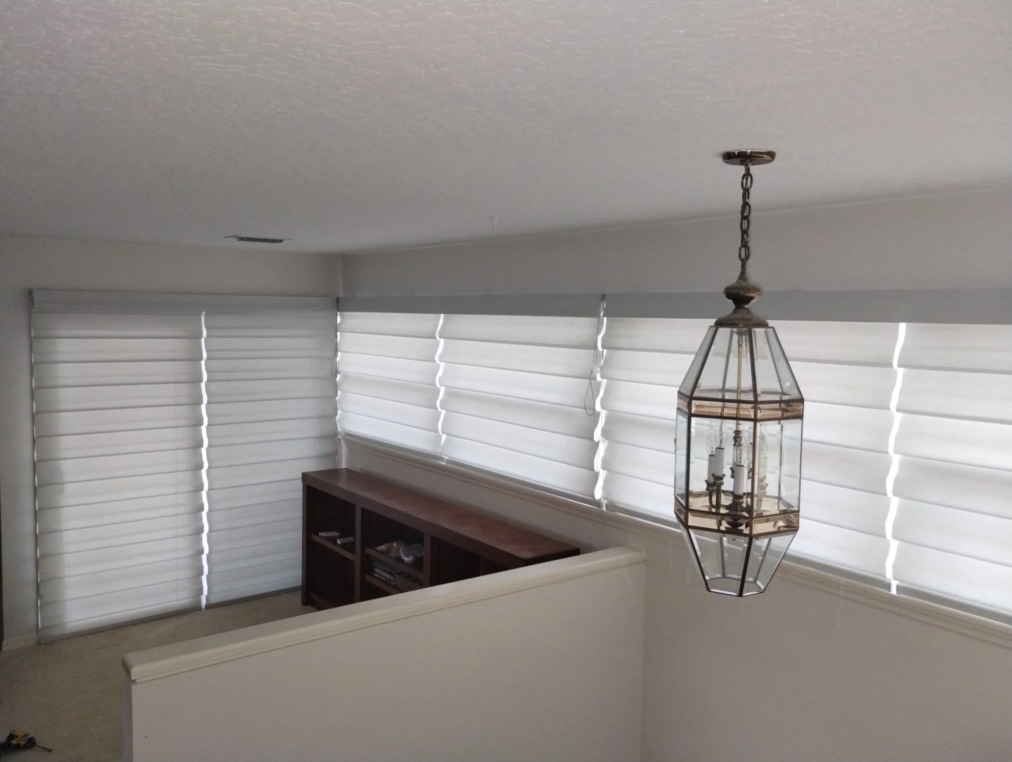 A room with white blinds covering windows, a hanging lantern-style light fixture, and a wooden shelf.