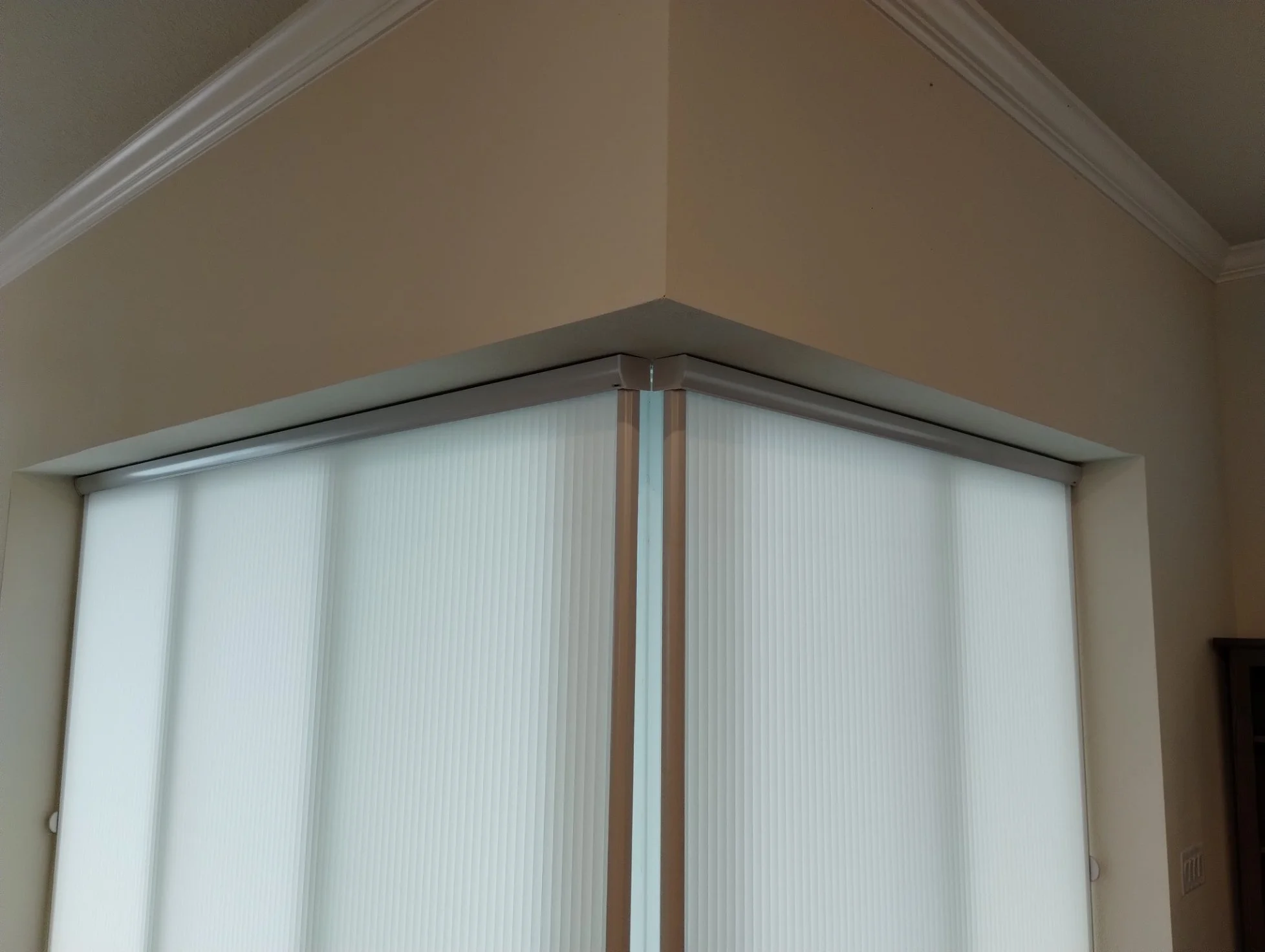 Close-up of window blinds covering a window, with beige walls and a white ceiling with crown molding.