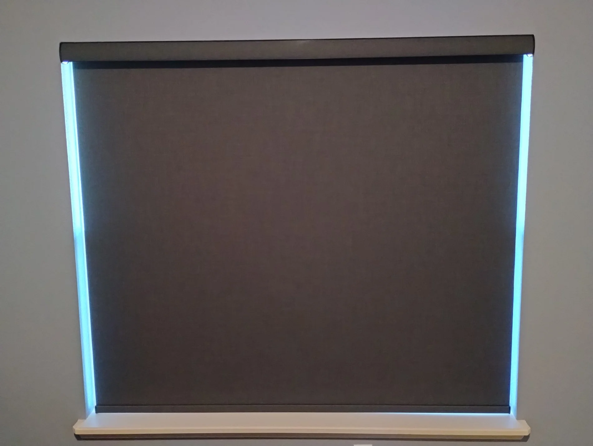 A rectangular display case with a dark interior, illuminated by blue LED lights along the edges, mounted on a white wall.