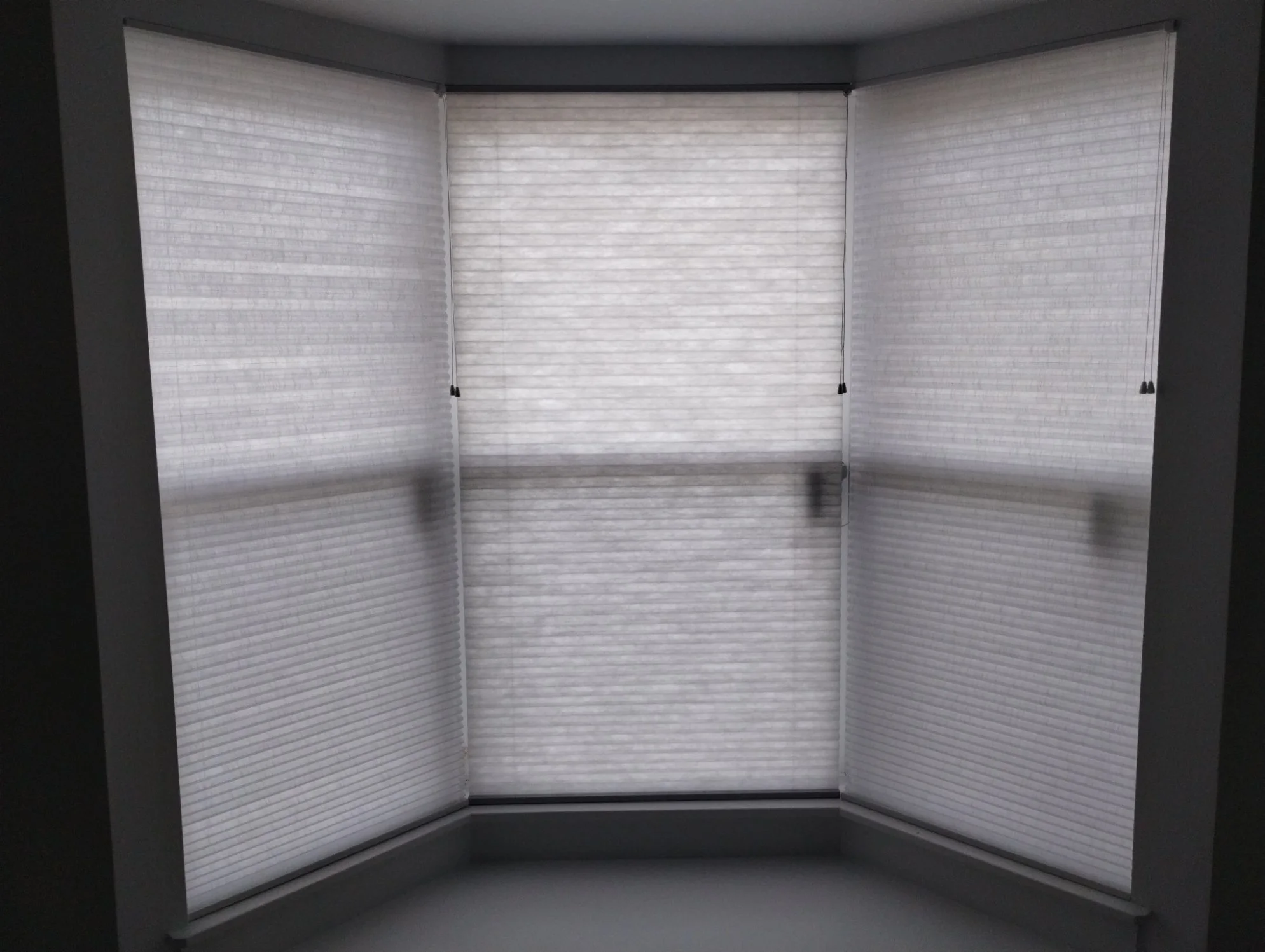 White shading blinds on a window or balcony door, partially open, with horizontal lines and black cords.