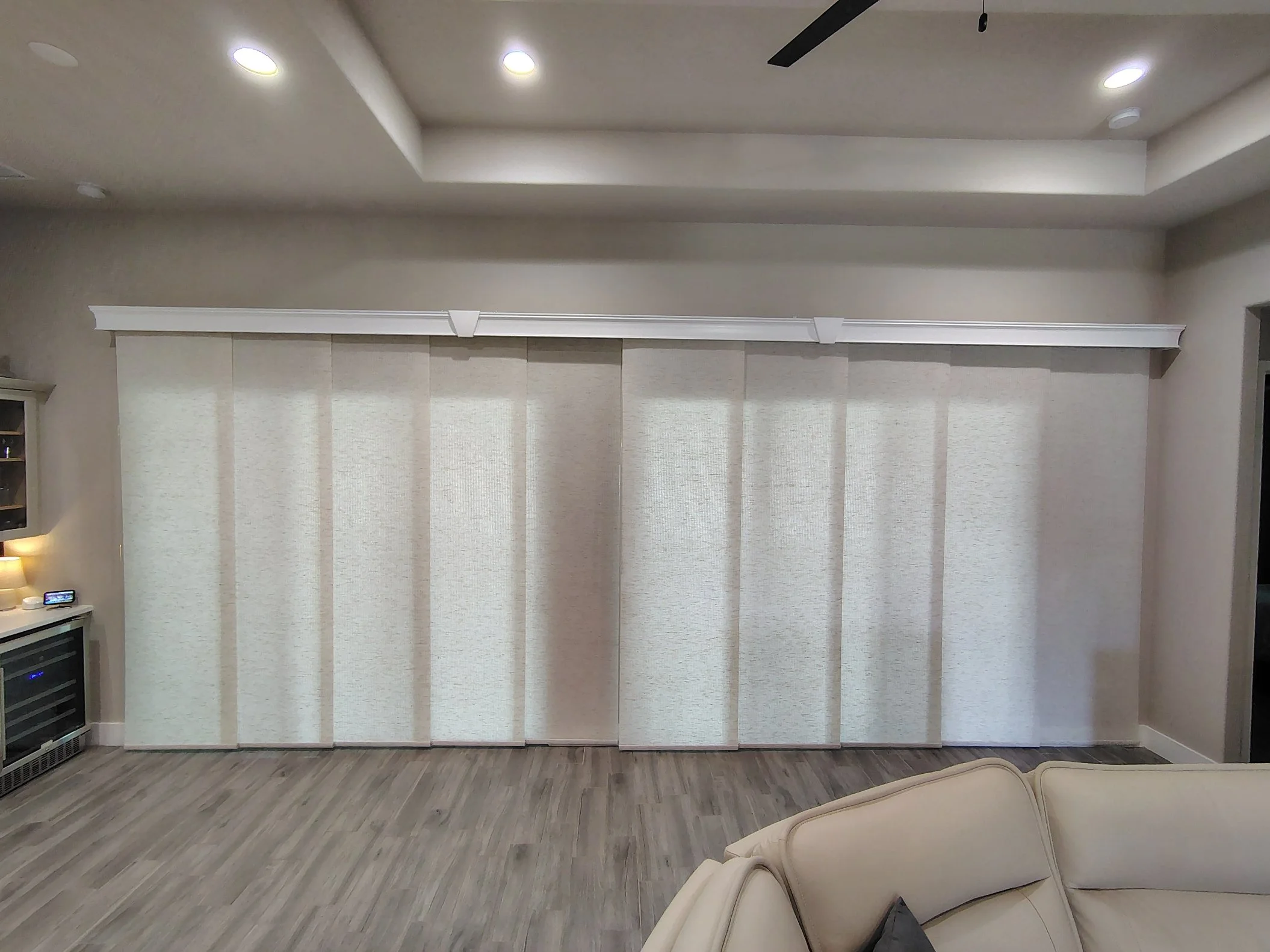 Living room with beige curtains on a window, a corner of a beige sofa, and a wood floor.
