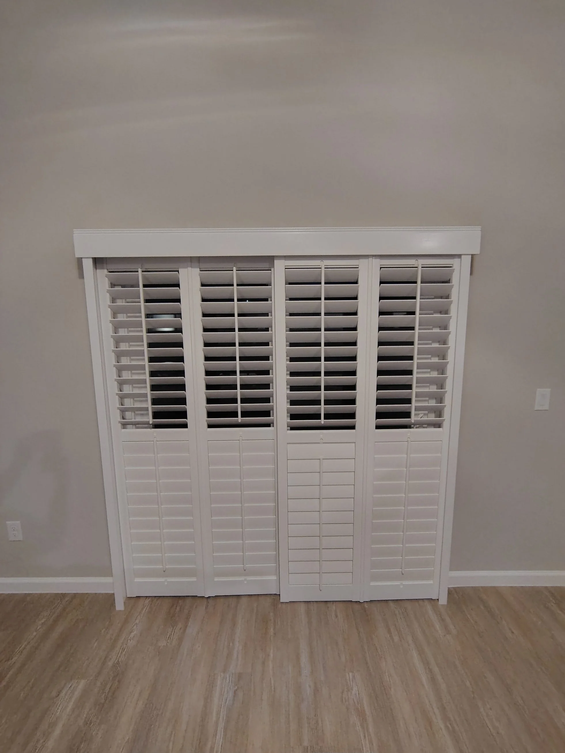 A white louvered closet door gathered against a plain gray wall with a white electrical outlet near the floor.