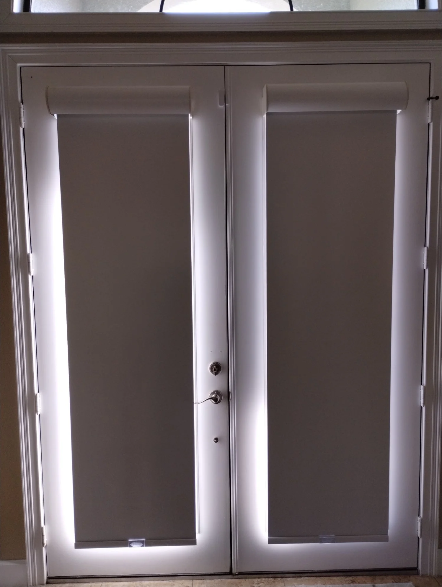 White double doors with rollers and a lock, set in a beige wall with a stone floor below.