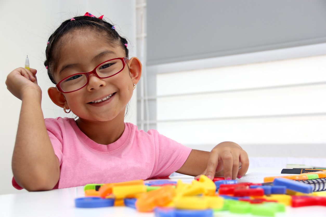 A young girl with glasses smiling while playing with colorful toys during language therapy for kids in Washington, DC.