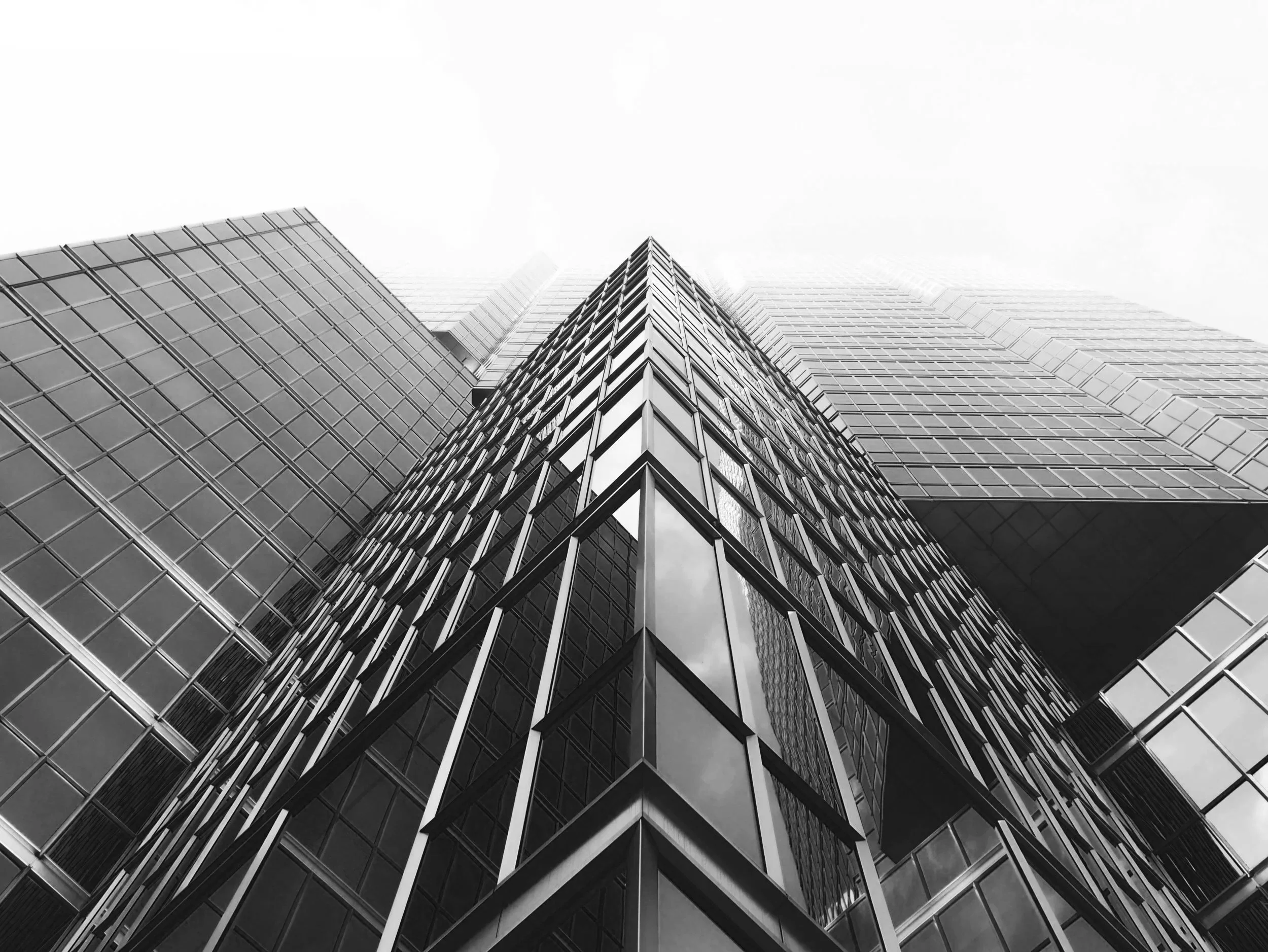 Low-angle view of a modern glass skyscraper with geometric patterning and reflective windows in grayscale.