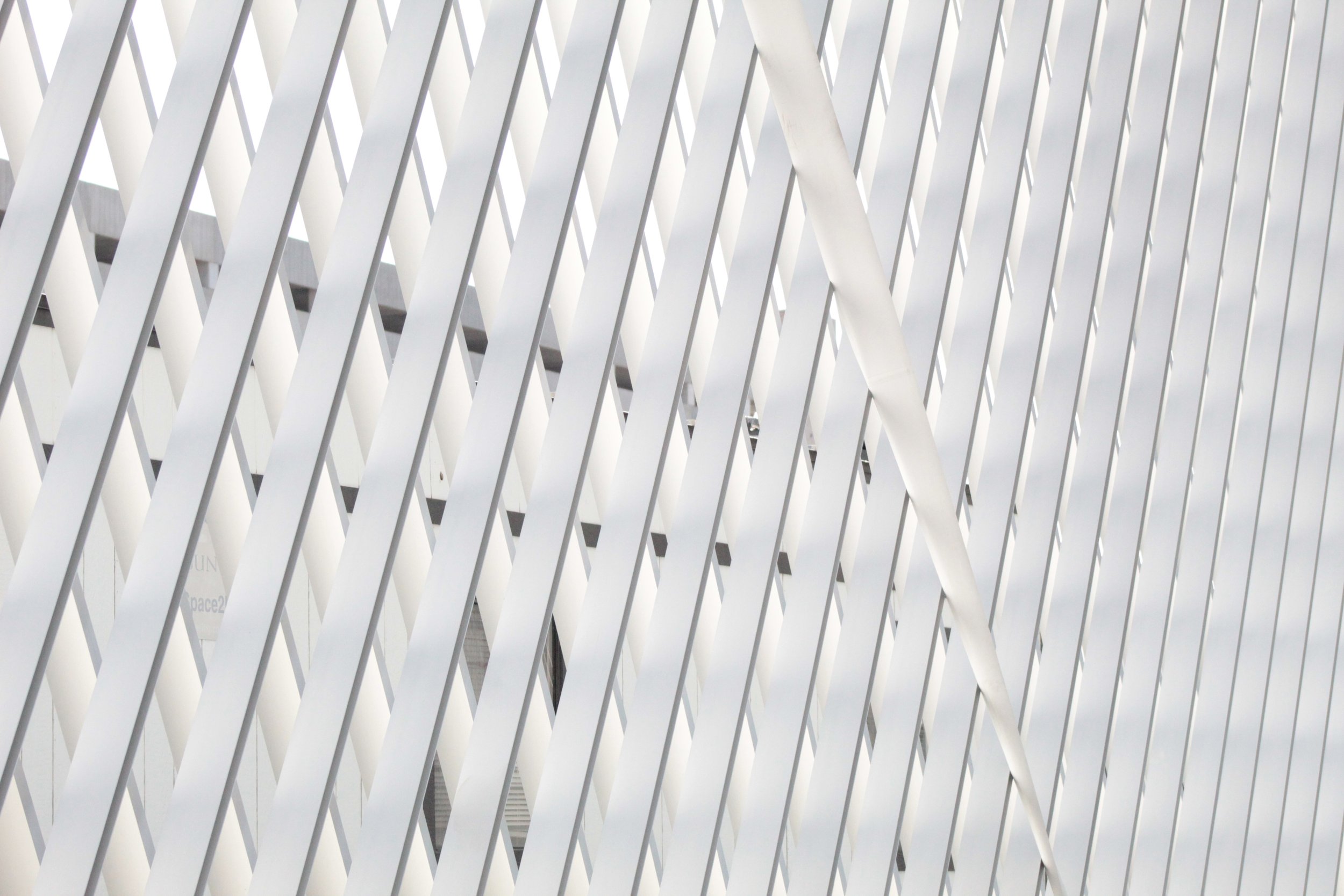 Close-up view of a white, modern architectural structure with diagonal slats creating a pattern of lines and shadows.