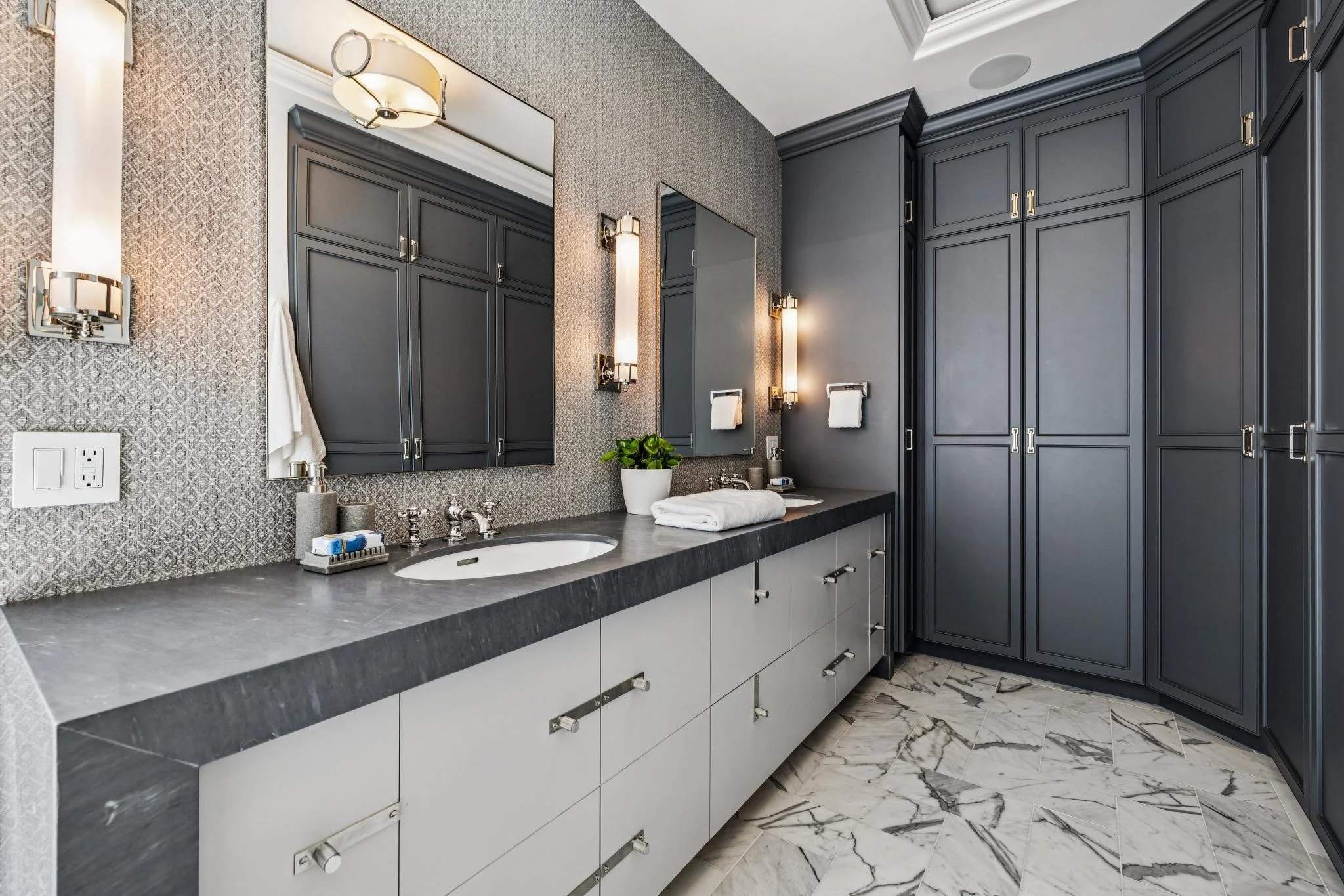A modern bathroom with a dark vanity, a large mirror, wall-mounted lights, and patterned tile flooring.