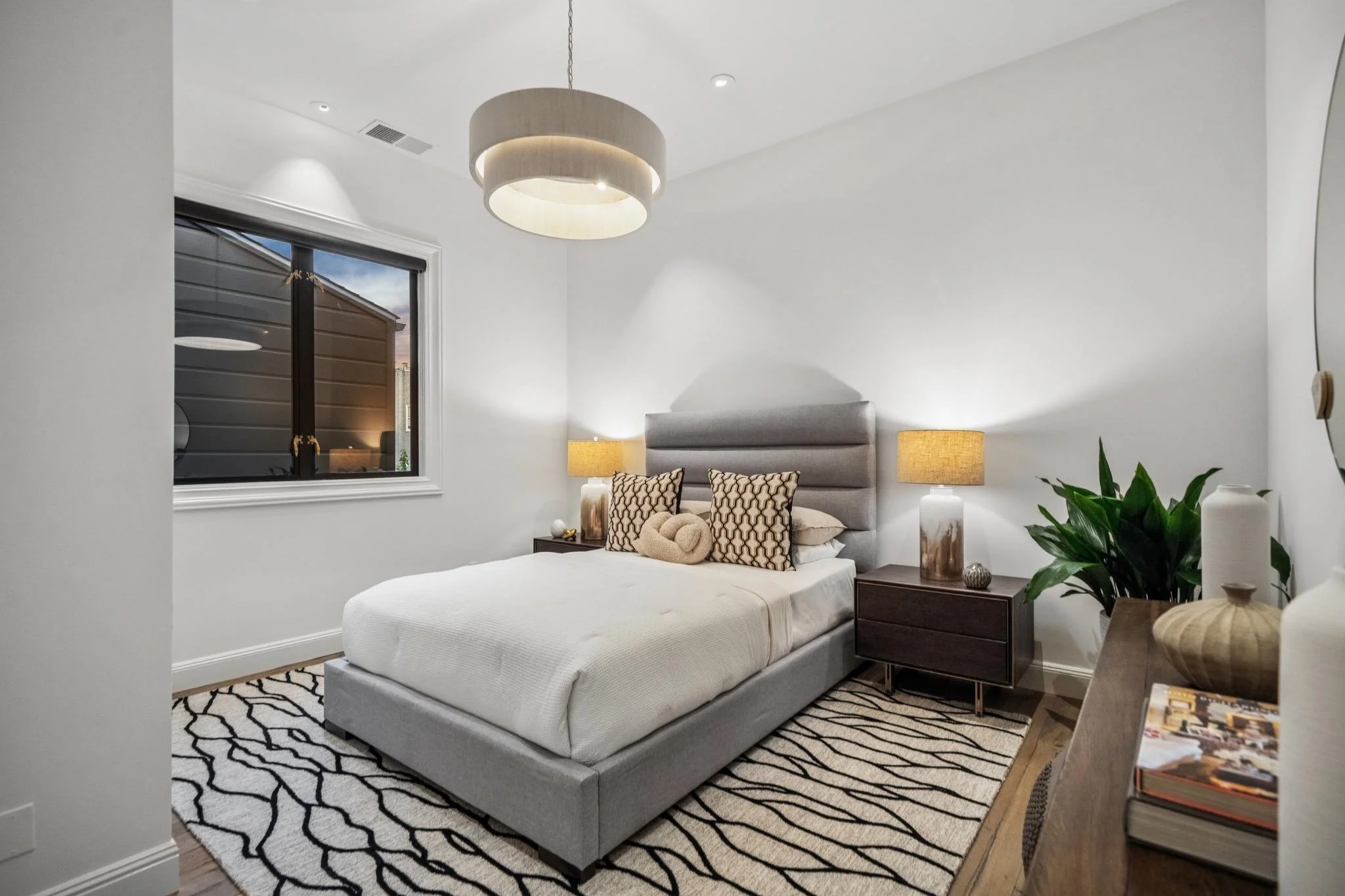 A bedroom with a bed, nightstands, lamps, a window, and a patterned rug.