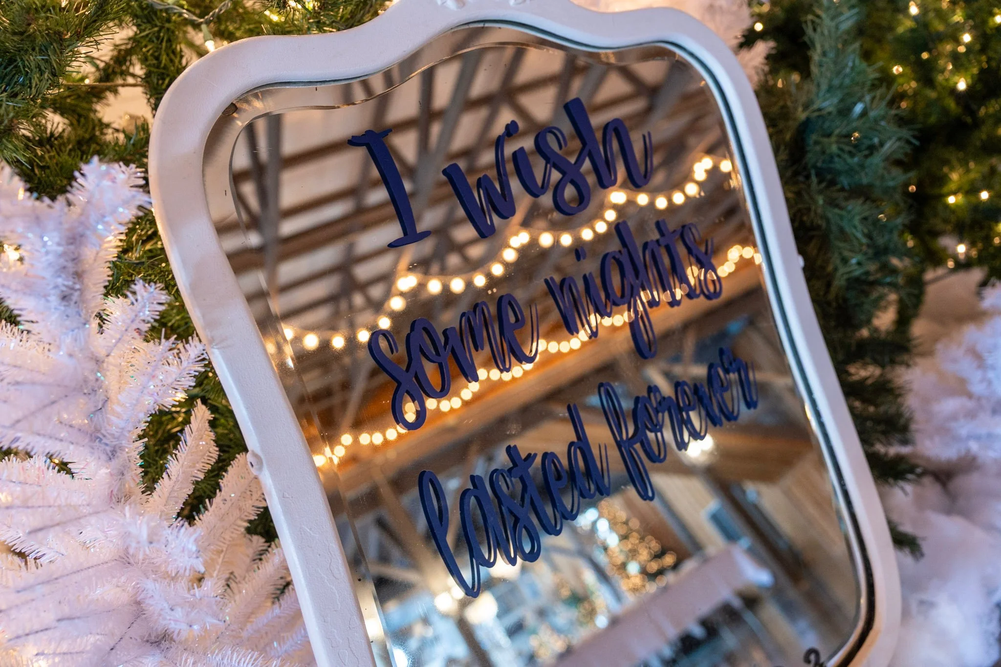 A decorated Christmas tree with a white ornament mirror with blue writing that says 'Happy New Year.'