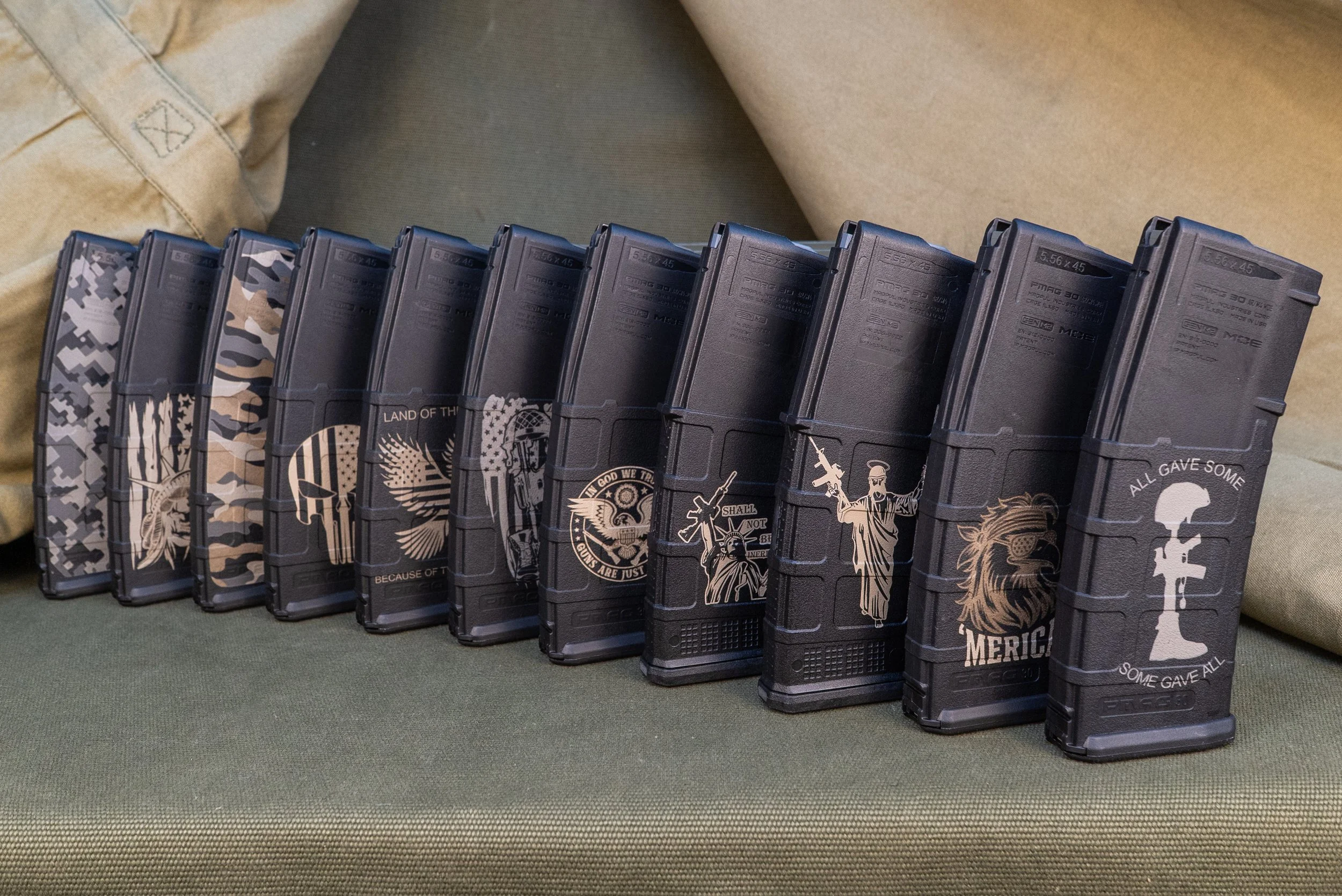 A row of black magazines engraved by Tactical Penguin with patriotic and military graphics, placed on a green surface with a beige fabric background.