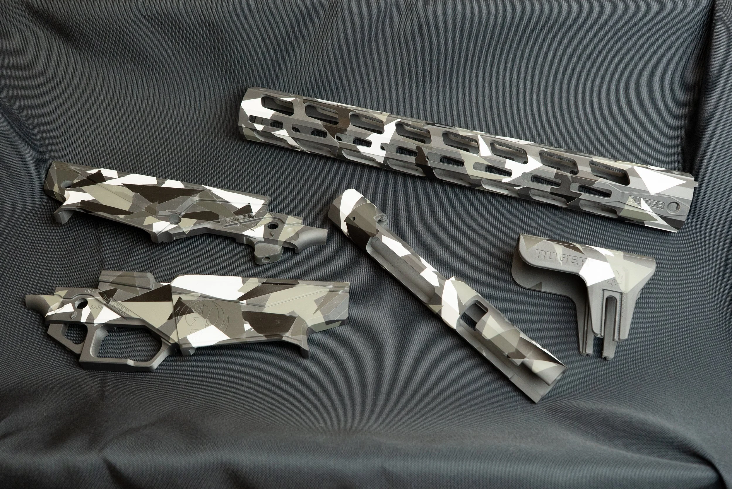 Multiple parts with a custom Cerakote camouflage pattern laid out on a black surface.