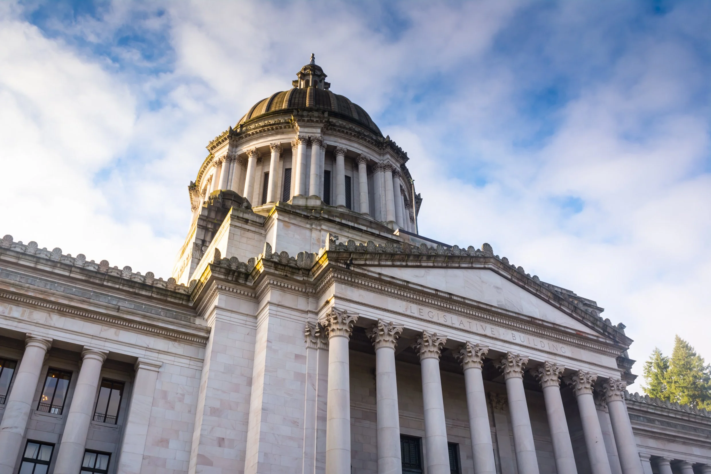 Close-up of a classical government building with a large dome, columns, and the word "Legislative" engraved on the front, set against a partly cloudy sky.