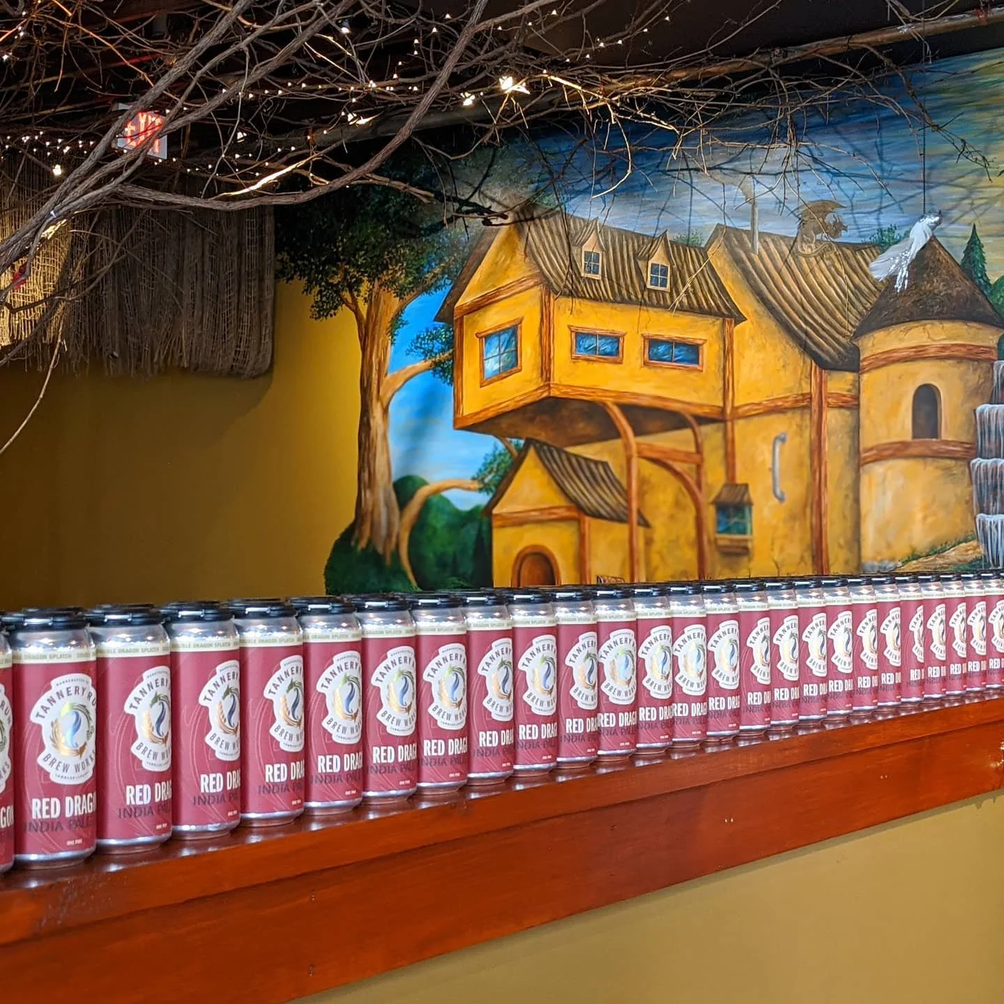 Shelf of Tannery Run beer cans with decorative mural background of a fantasy castle scene.
