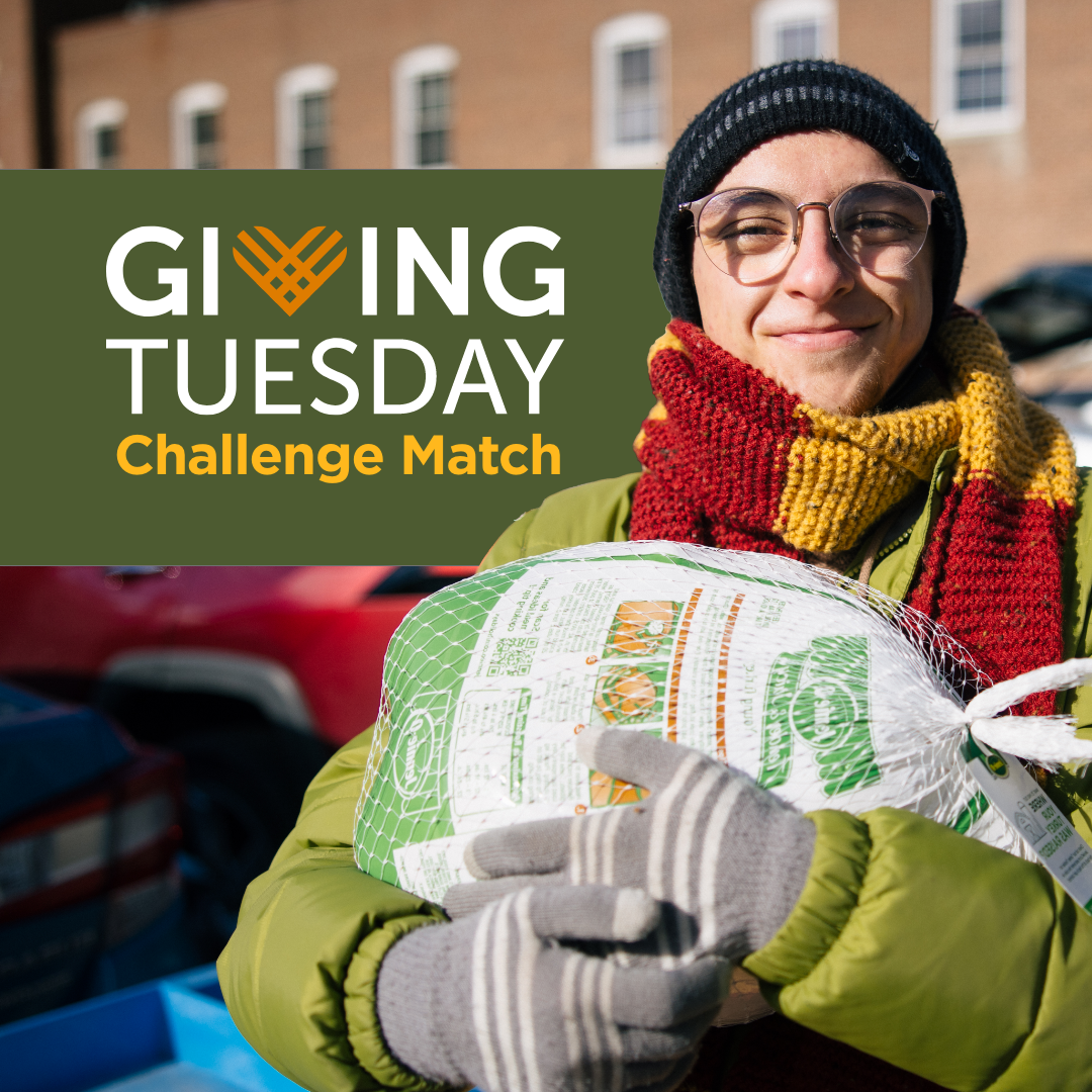 A smiling woman wearing glasses, a black beanie, and a red and yellow scarf, holding a bag of food outdoors with cars and a brick building in the background, promoting Giving Tuesday Challenge Match