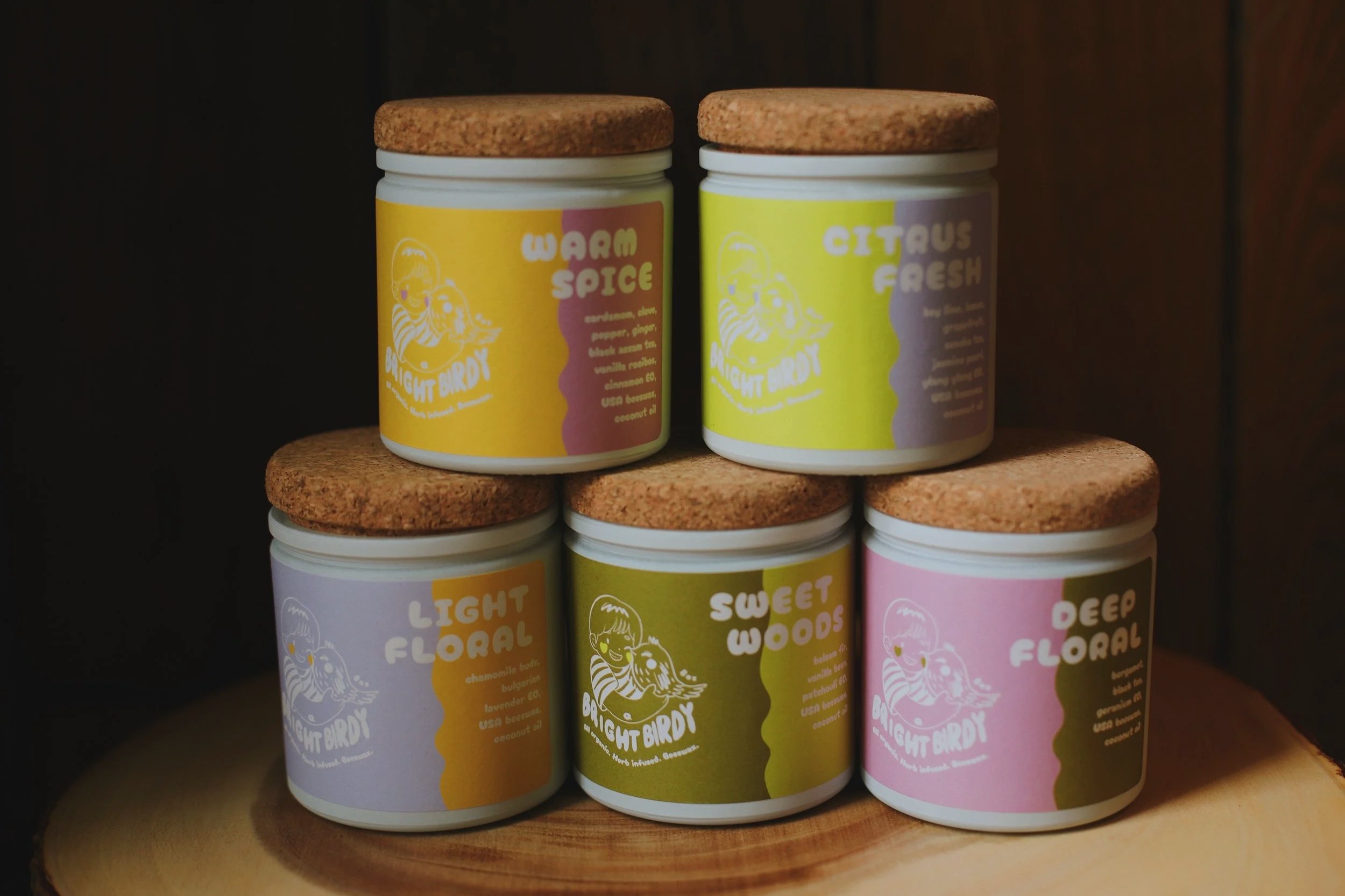Stack of jars with colorful labels and cork lids on a wooden shelf.