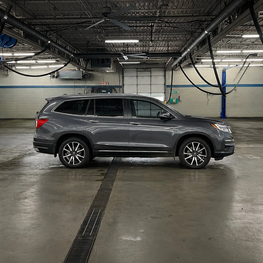 A gray Honda Pilot parked in an automotive shop with a concrete floor and exposed piping on the ceiling.
