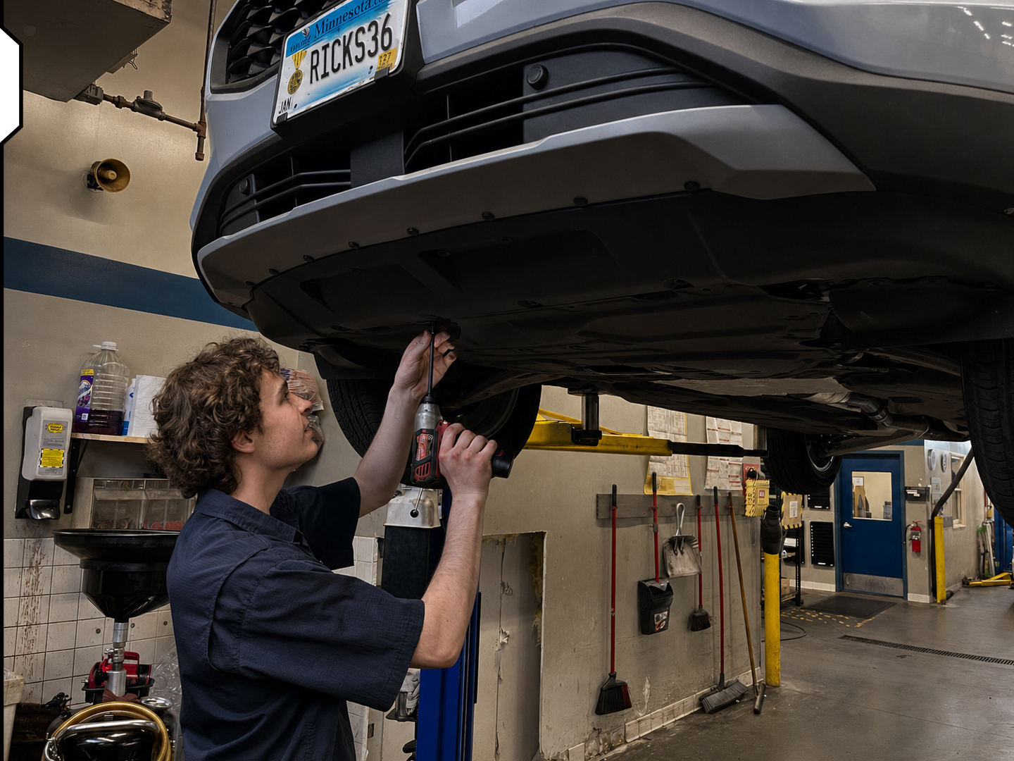 A mechanic working underneath a car in a garage, using a tool to perform maintenance.