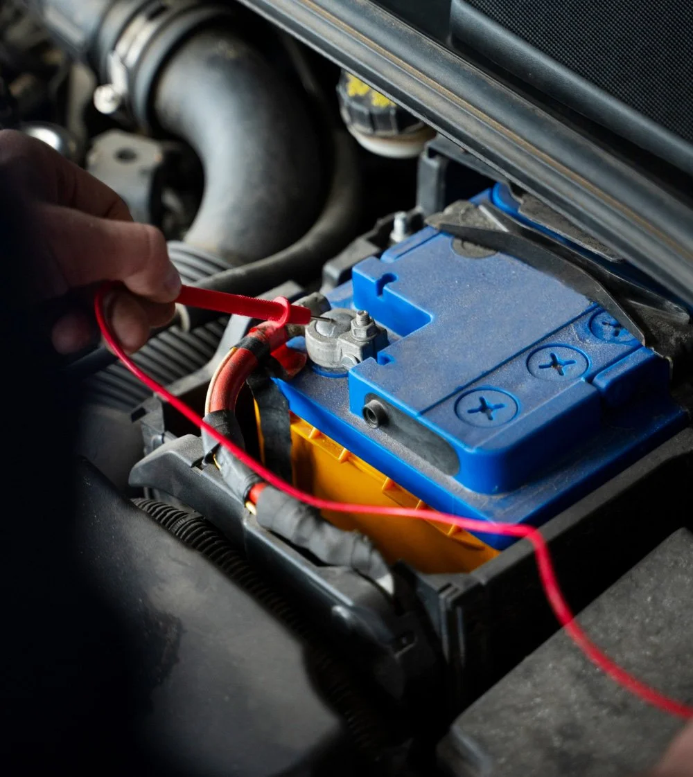 A person using a red probe to check a car battery under the hood.