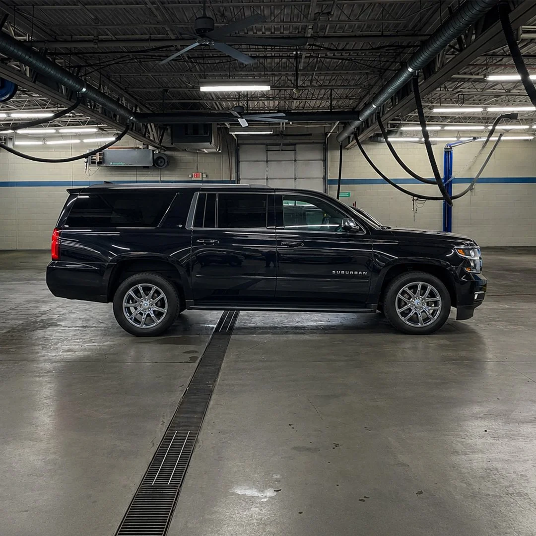 Black Chevy Suburban parked inside a garage or automotive shop with industrial ceiling and lighting.