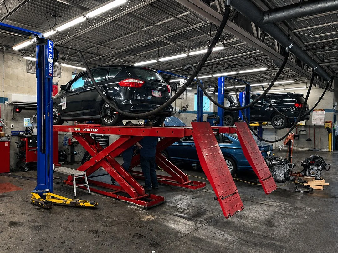 Automotive repair shop with cars on hydraulic lifts and mechanics working underneath, tools and engine parts scattered around.