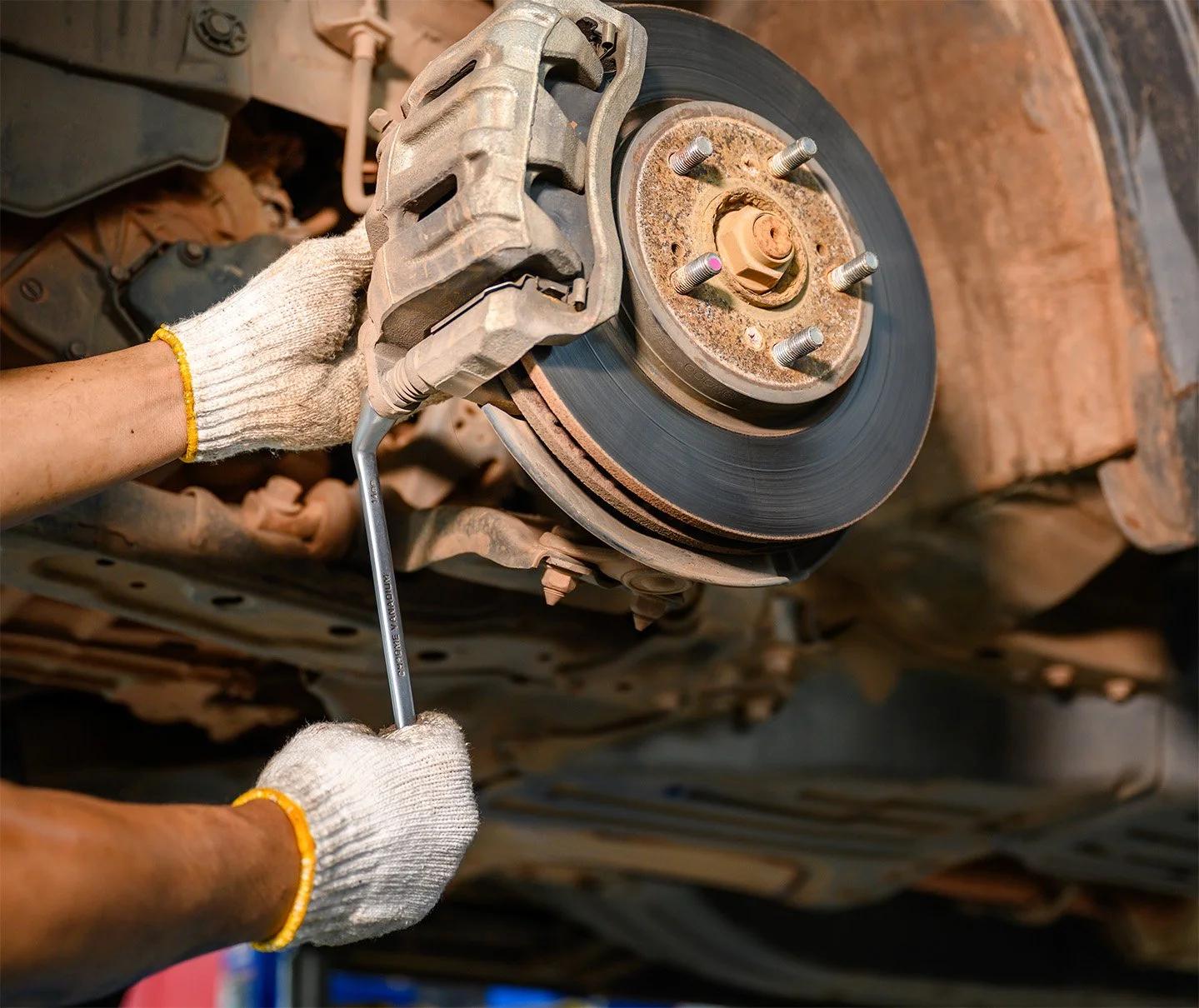 Mechanic installing new brake rotor and caliper on a vehicle's wheel hub.