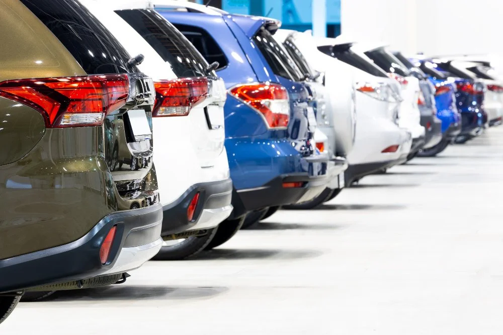 Line of various parked cars in an indoor parking garage, showing rear views.