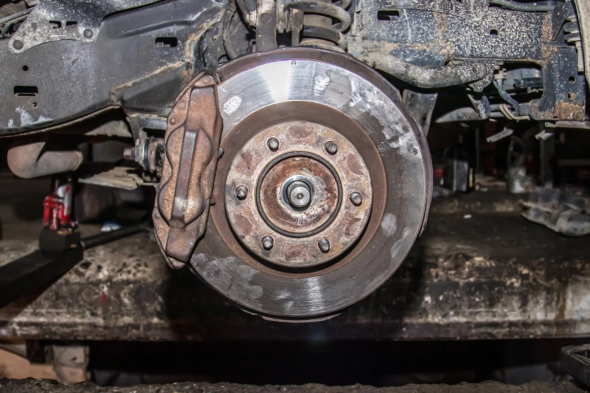 Close-up of a car's rear wheel area with the wheel removed, showing the brake rotor, caliper, and suspension components.