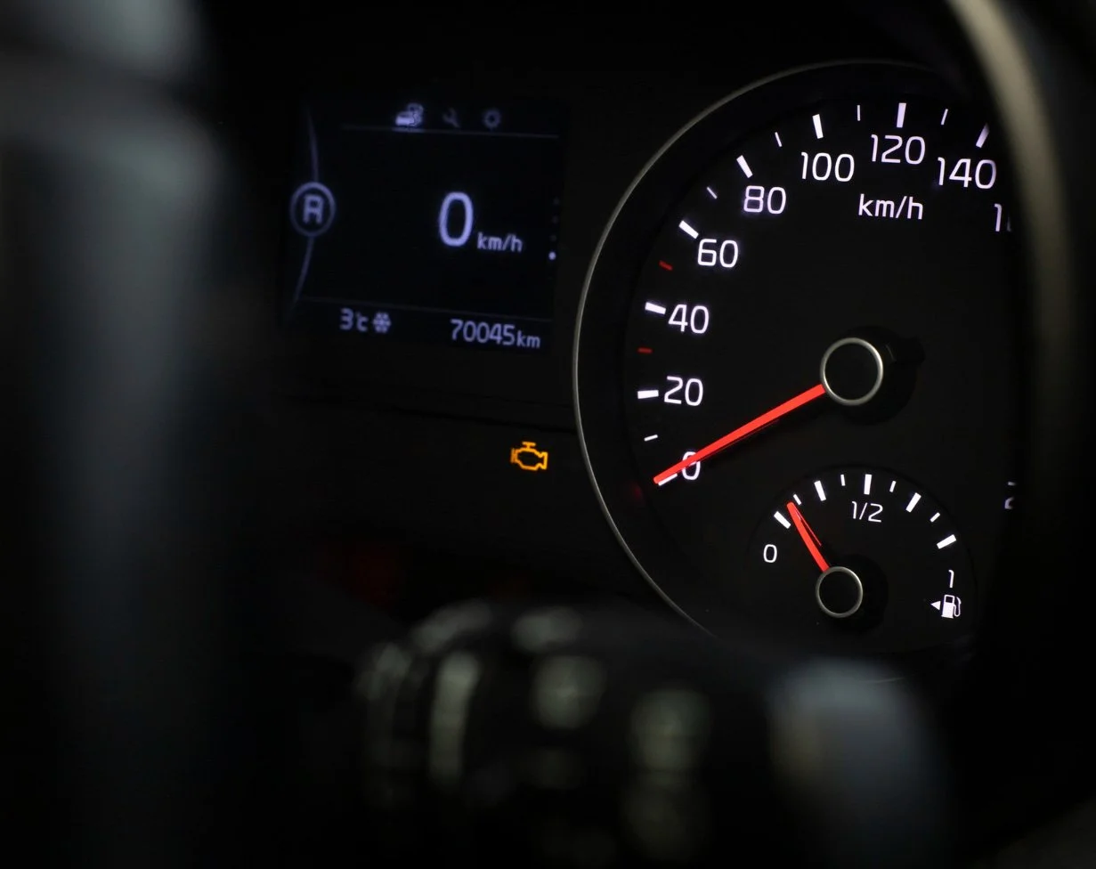 Car dashboard with speedometer, fuel gauge, and warning lights, including a check engine light.