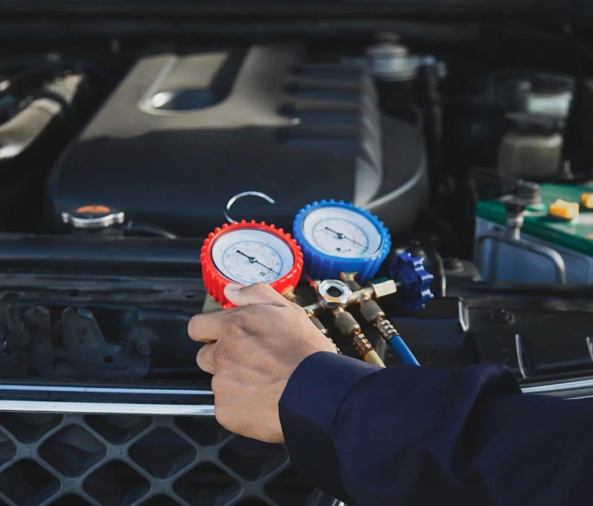 Person using manifold gauges to check car's air conditioning system under the hood.