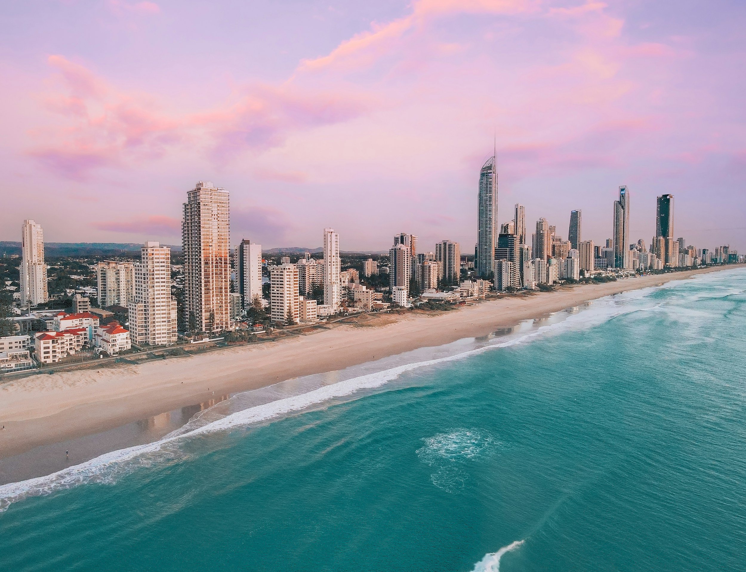Skyline of a coastal city with high-rise buildings along a beach at sunset
