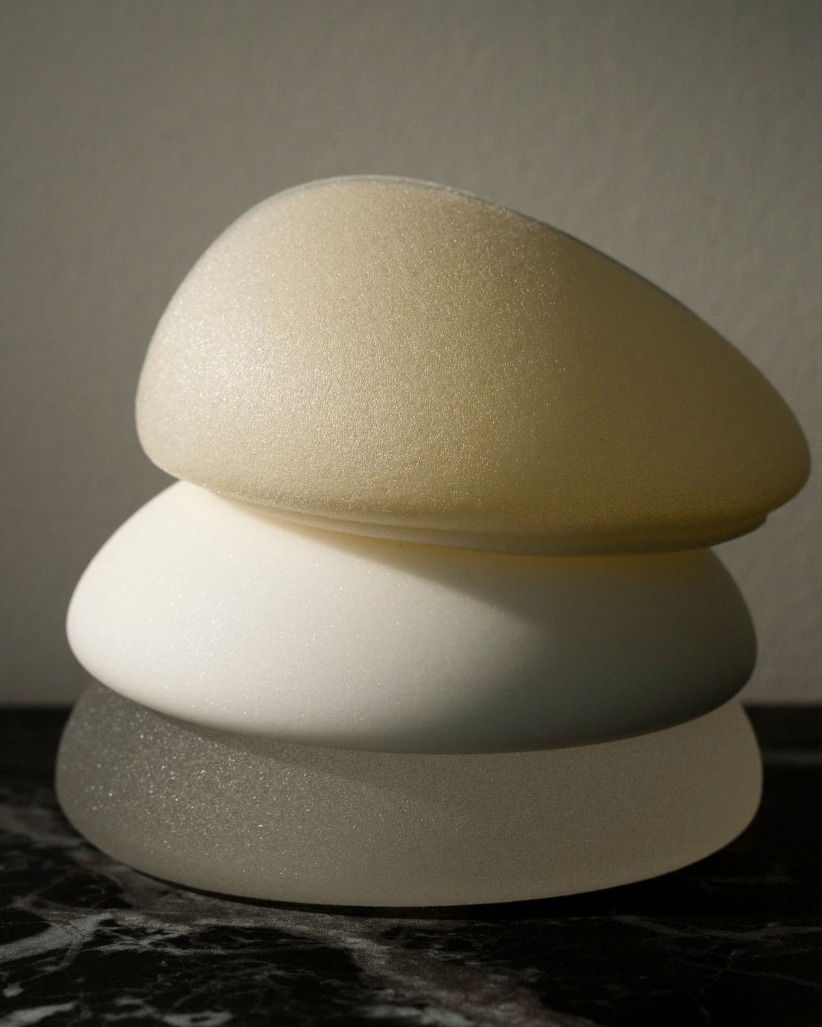 Close-up of four smooth beach stones stacked on top of each other, with the top stone in a golden color, the second in white, the third in gray, and the bottom in black, against a neutral background.
