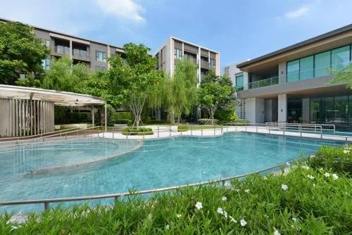Modern outdoor swimming pool surrounded by trees and modern apartment buildings with glass balconies during daytime.