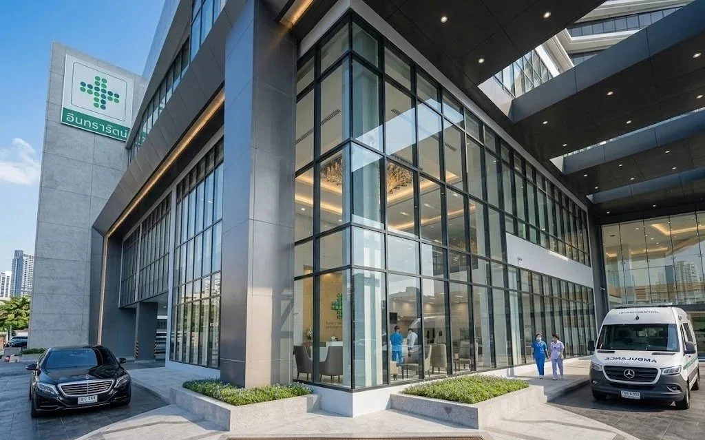 Modern hospital building with glass facade, parked cars, and medical staff outside.